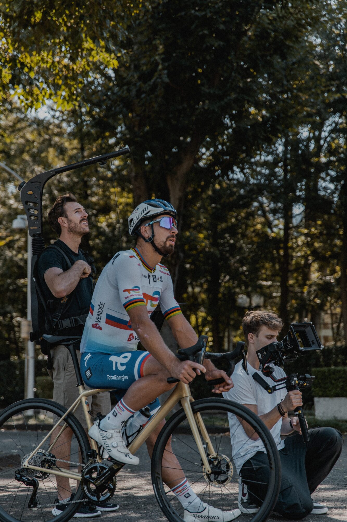 Person riding a bicycle with a helmet, accompanied by two people, outdoors with trees in the background.