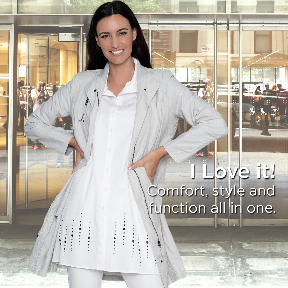 Smiling woman in white coat and dress standing in front of glass doors at an airport, hands on hips.
