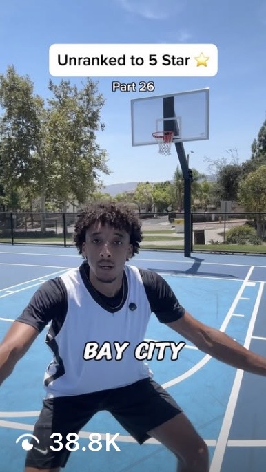 Young person in a basketball jersey on an outdoor court, with a basketball hoop and trees in background.