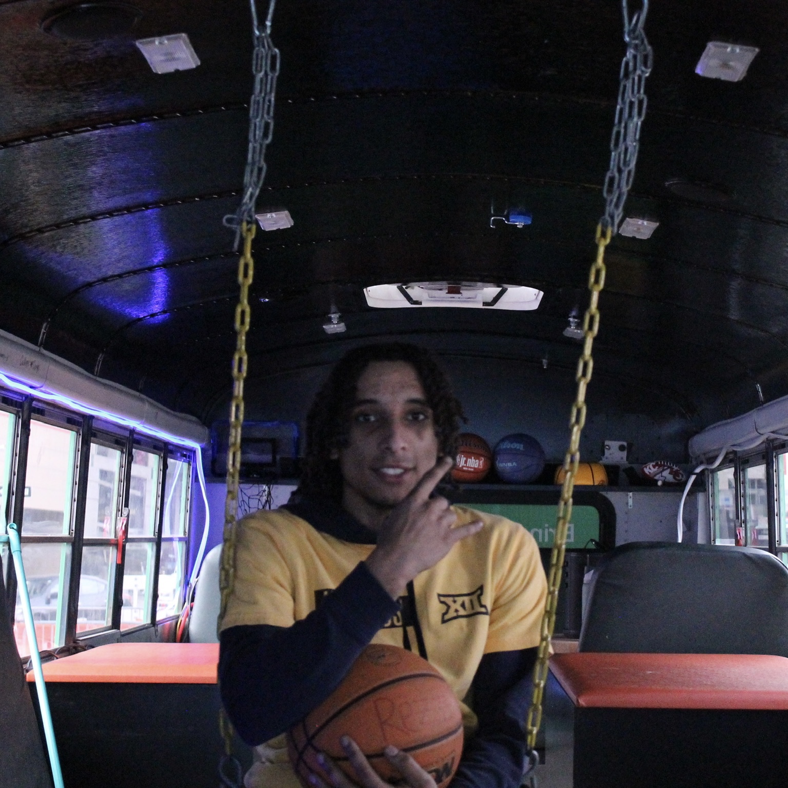 Person sitting on a swing inside a gym, holding a basketball, with gym equipment in the background.