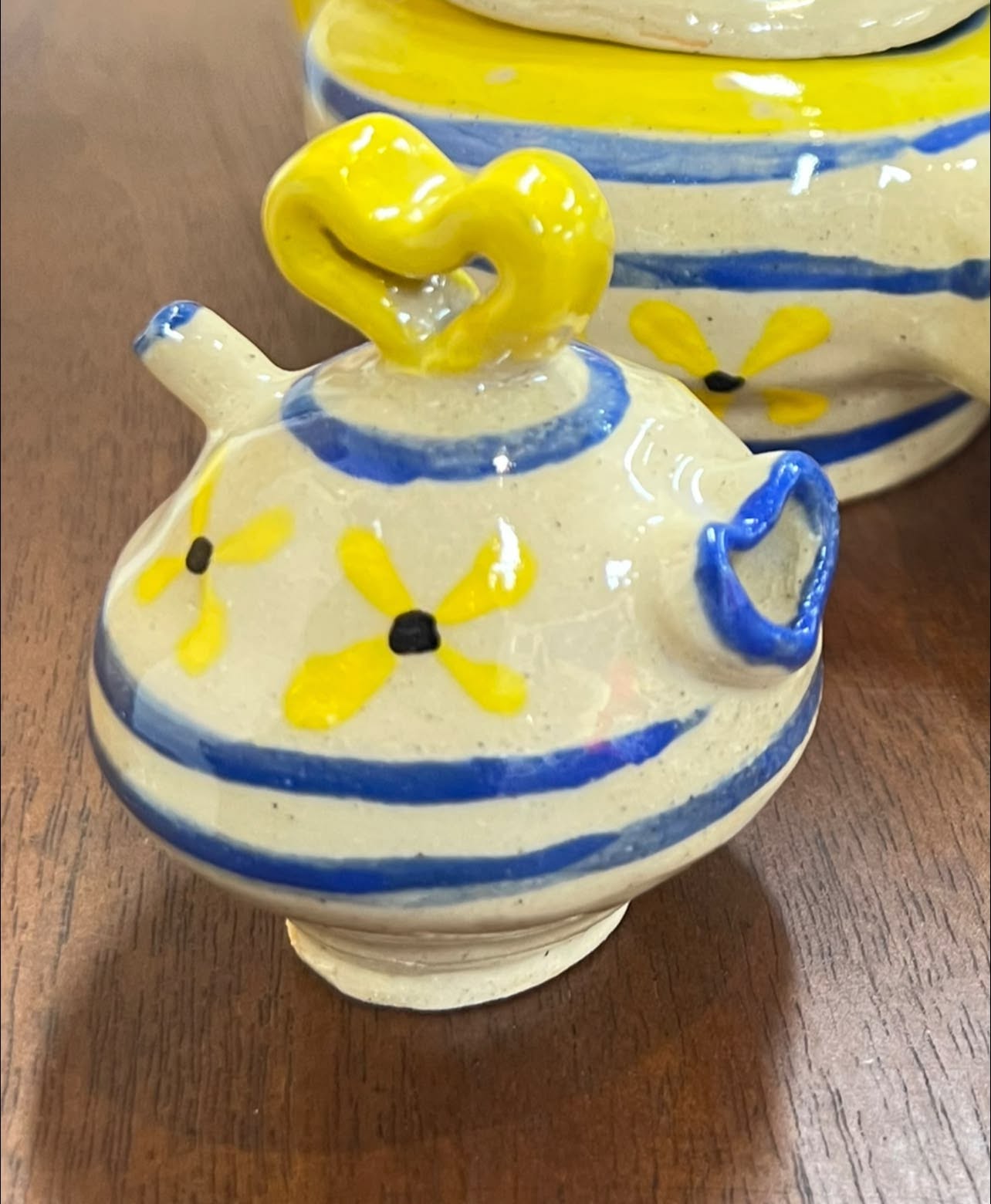 Decorative ceramic teapot with yellow and blue floral patterns and a yellow handle, placed on a wooden surface.