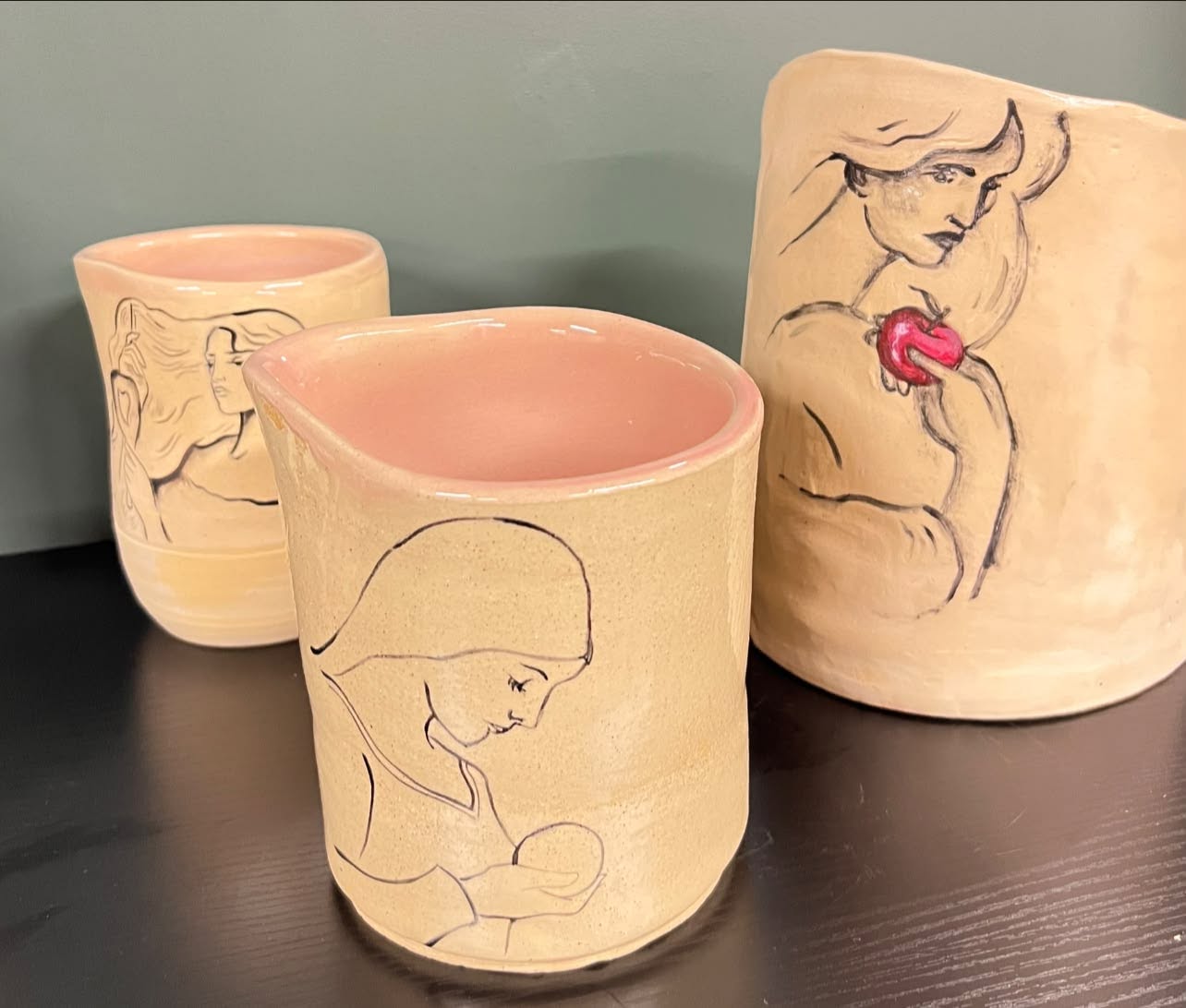 Three ceramic planters with line art drawings of women, one holding a pink heart-shaped object, on a black surface.