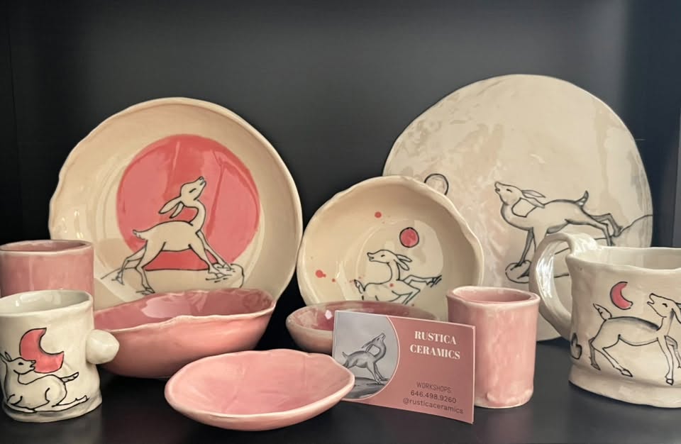 Collection of ceramic dishes and cups with animal illustrations, pink and white colors, and a business card, displayed on a dark surface.