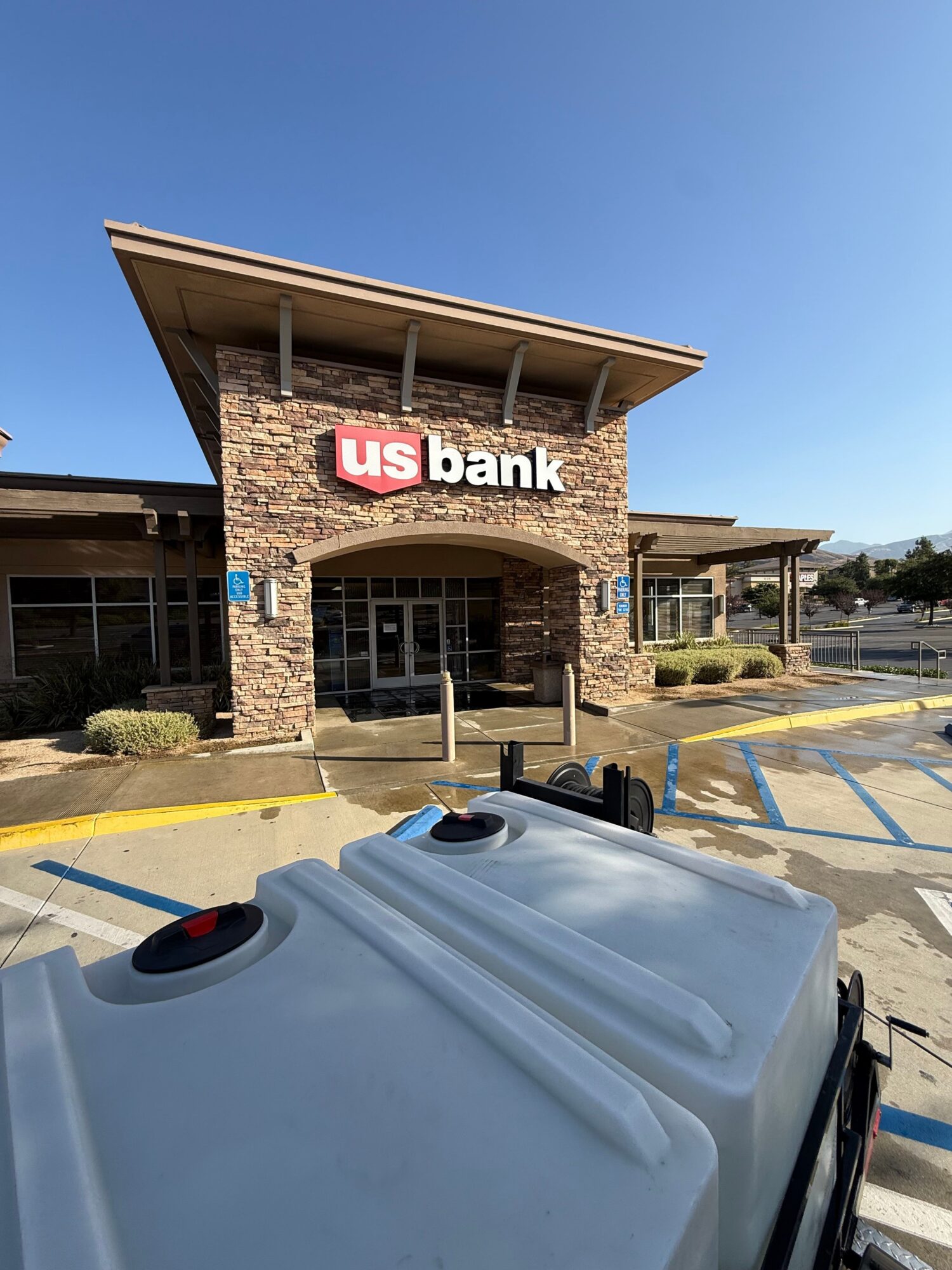 US Bank branch with brick exterior and sign, parking lot in front, vehicle partially visible, clear blue sky.