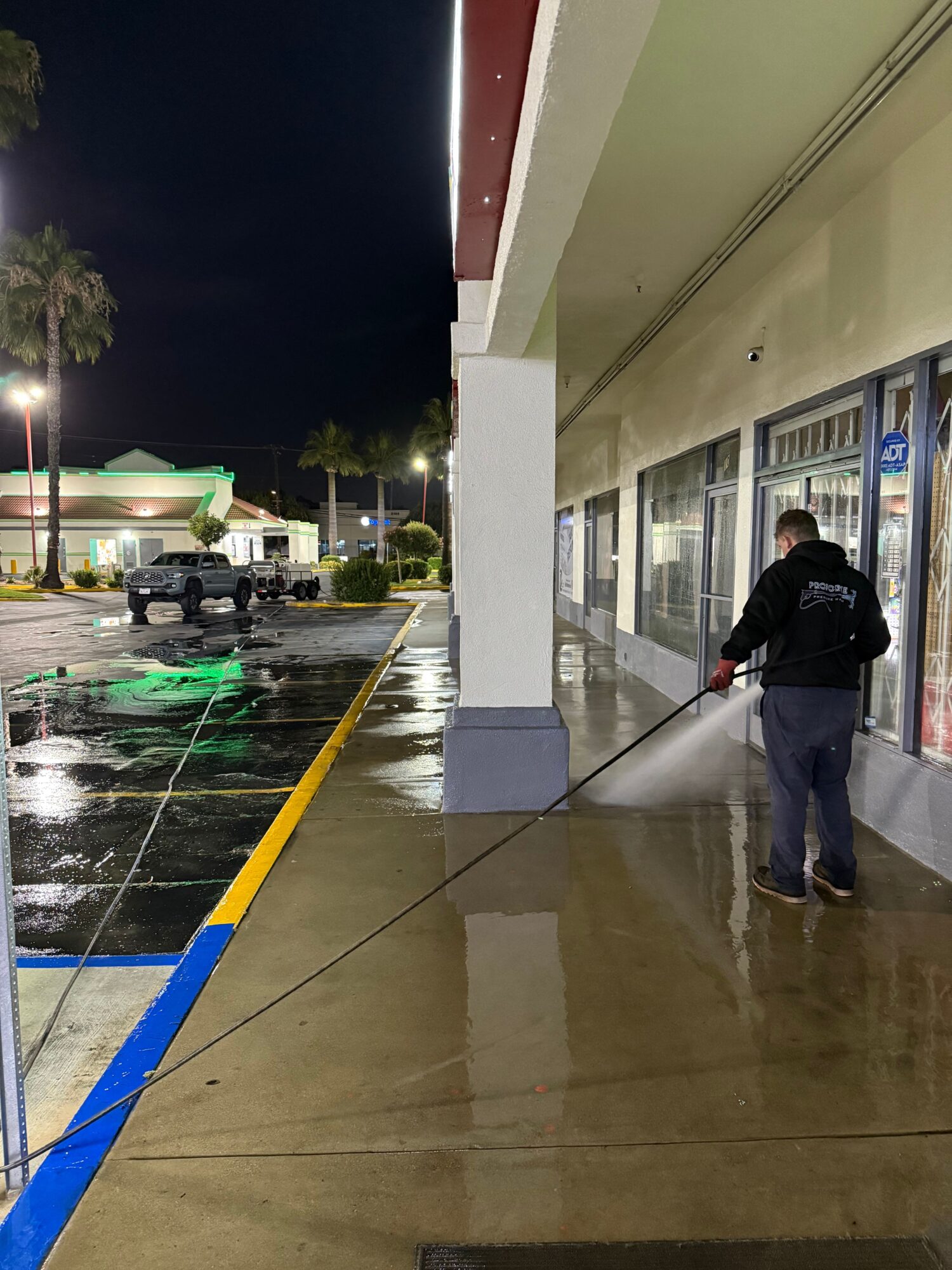 Person cleaning floor with a mop in a store aisle at night, illuminated by store lights, with shopping carts nearby.
