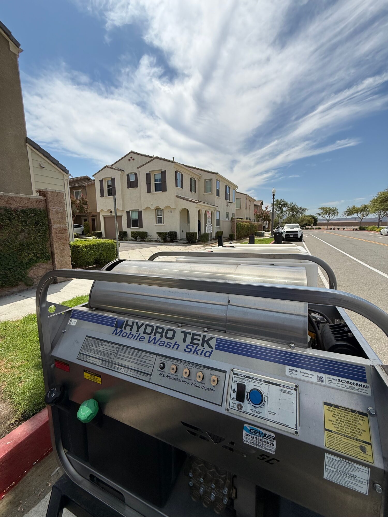 Street view with buildings, blue sky, and clouds, seen from a cart with equipment, on a sunny day.