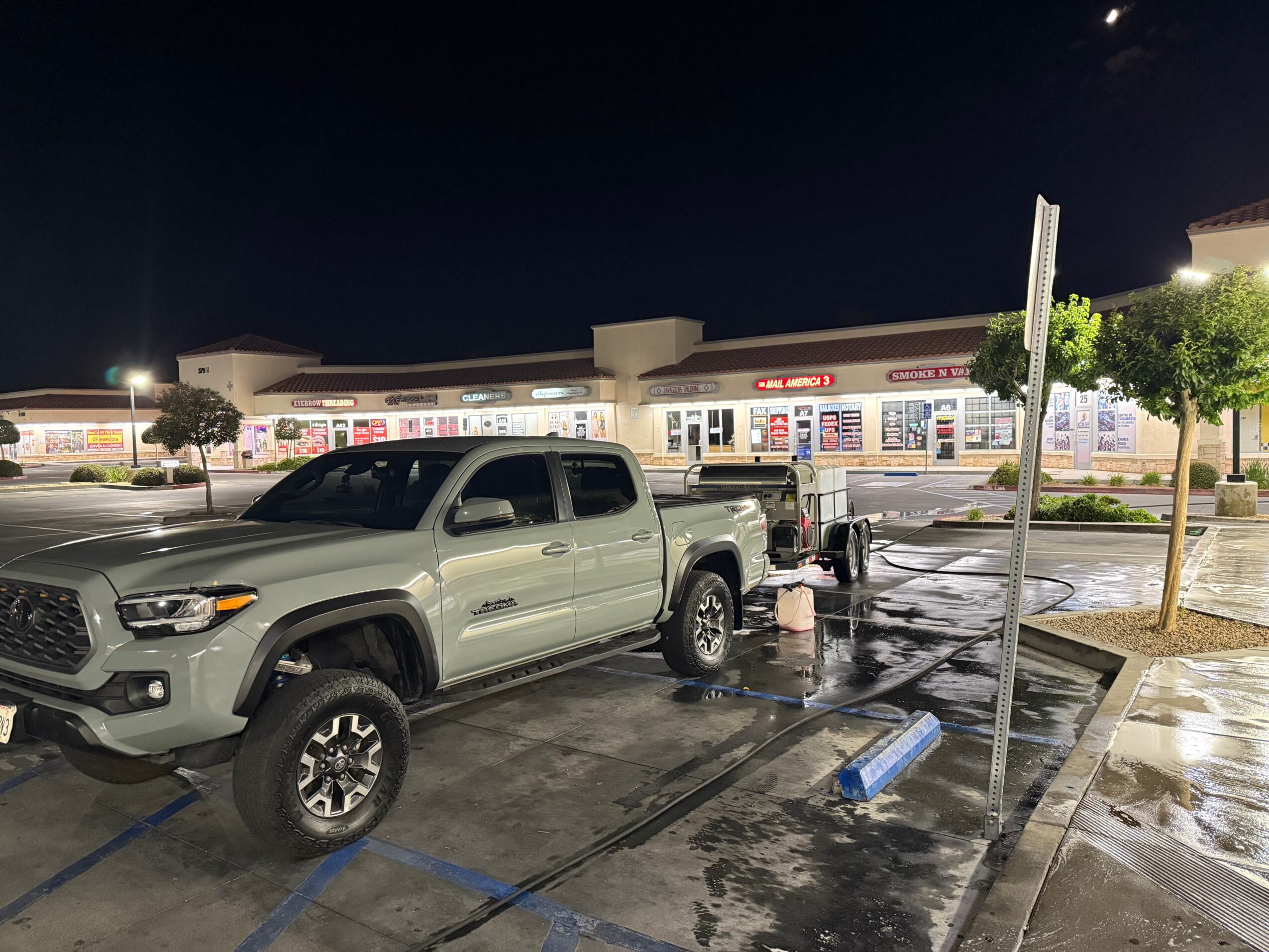 Gray pickup truck parked in a wet parking lot at night with a shopping center in the background.