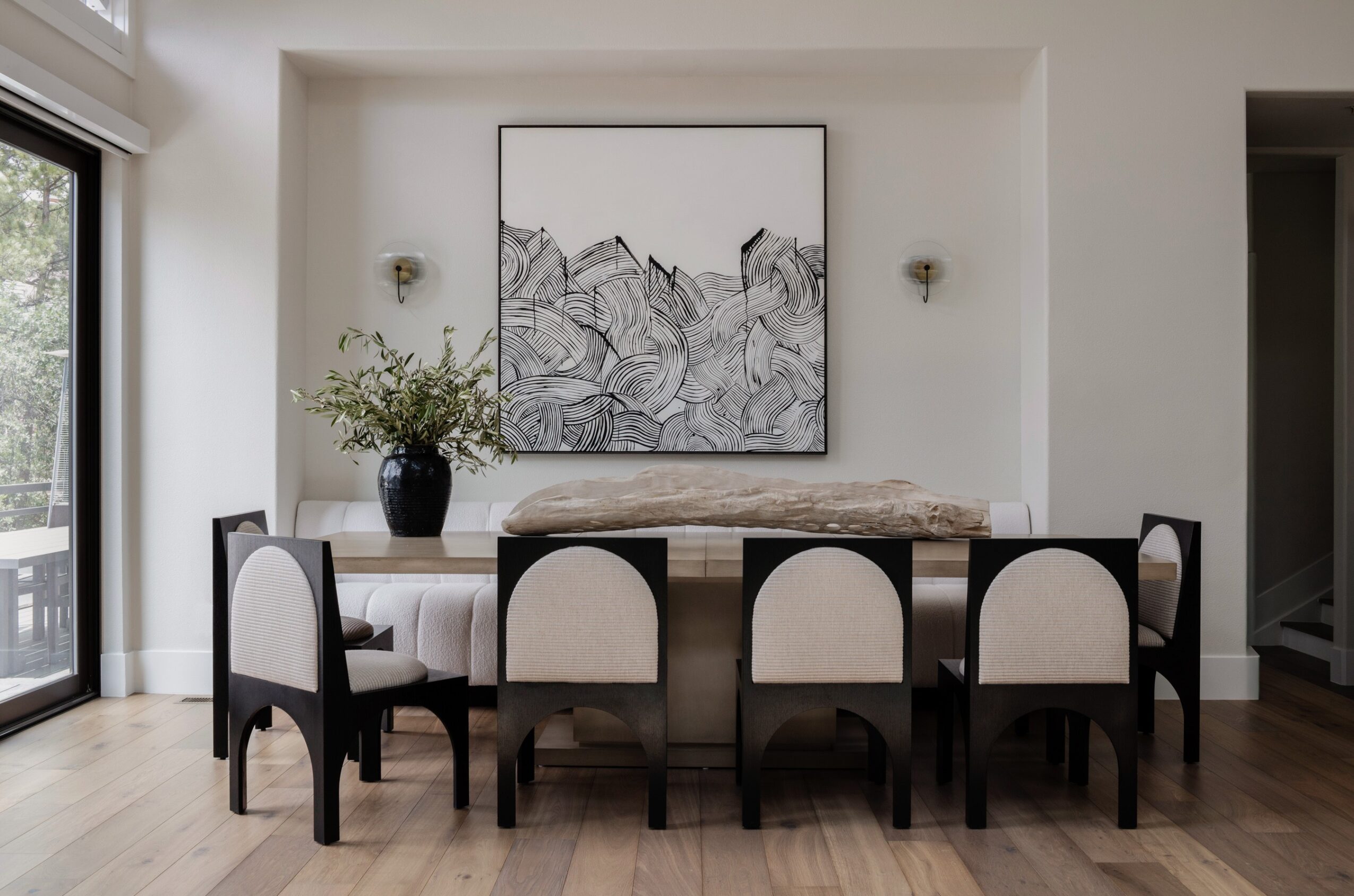 Dining table with six chairs, artwork, and a vase with greenery on the table, in a bright room with a sliding door.