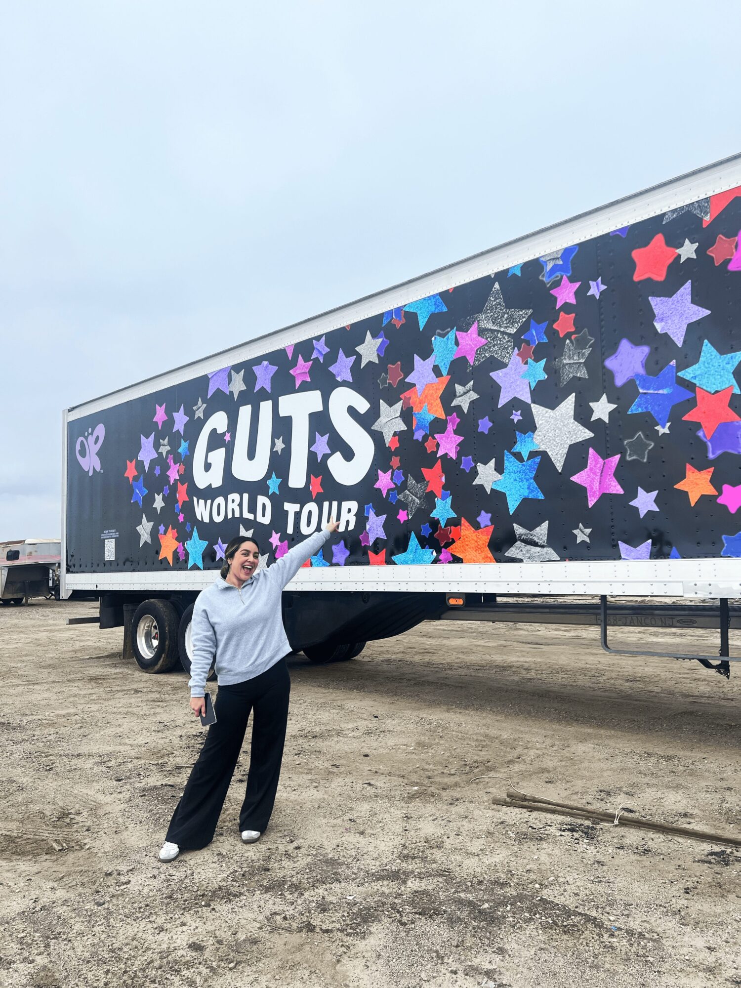 Person standing outdoors near a large truck with colorful star patterns and text, cloudy sky in background.