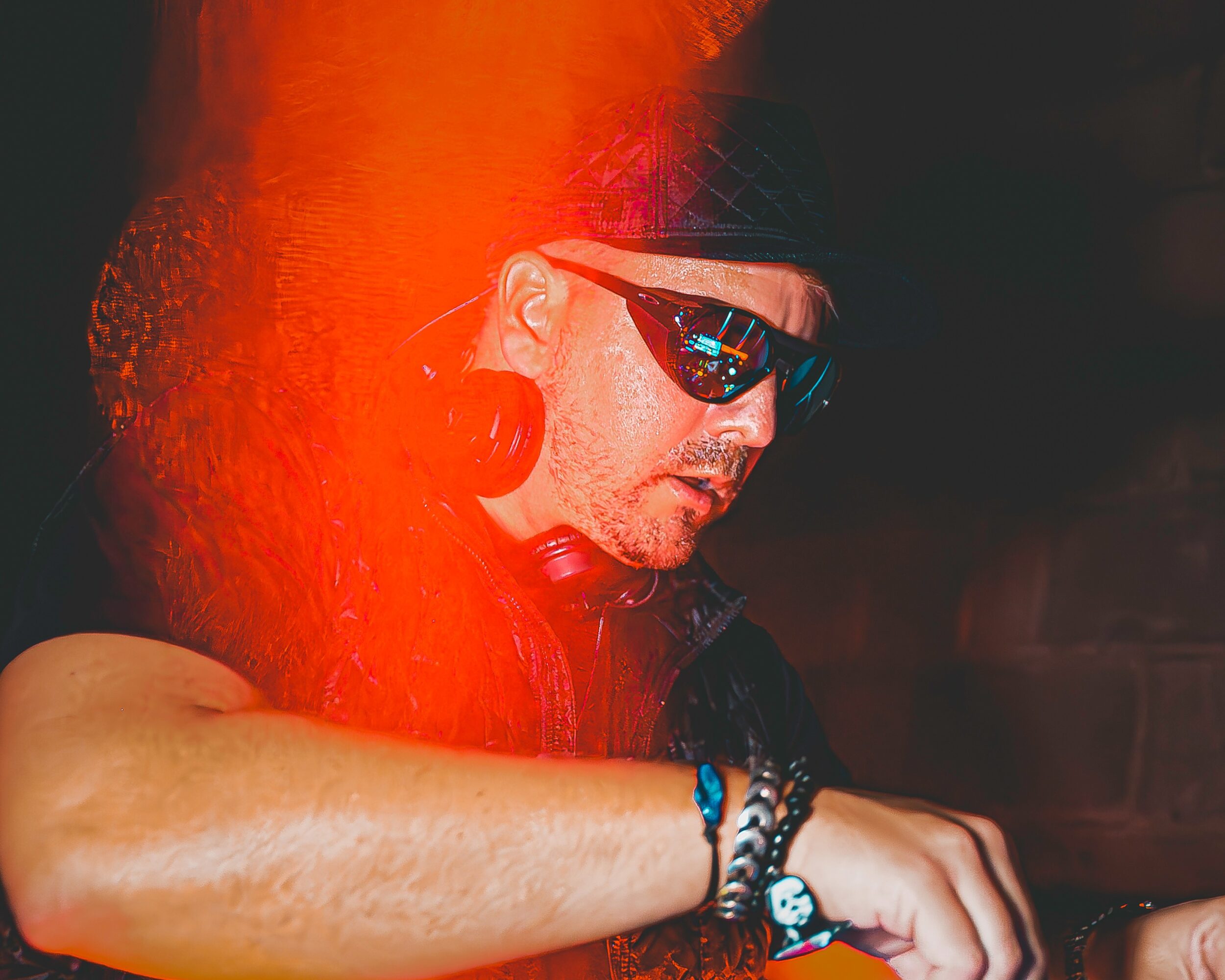 Person with curly hair wearing sunglasses and a black headband, focused on something in front, with a dark background.