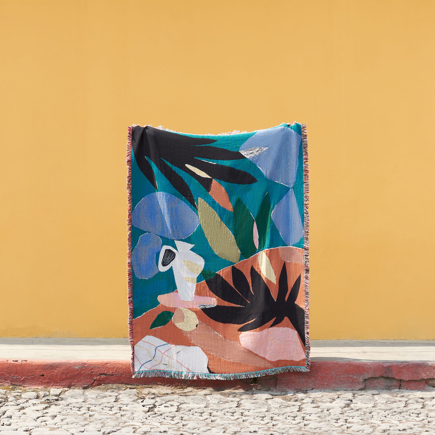 A colorful abstract painting on a canvas leaning against a yellow wall, with a sidewalk in front.