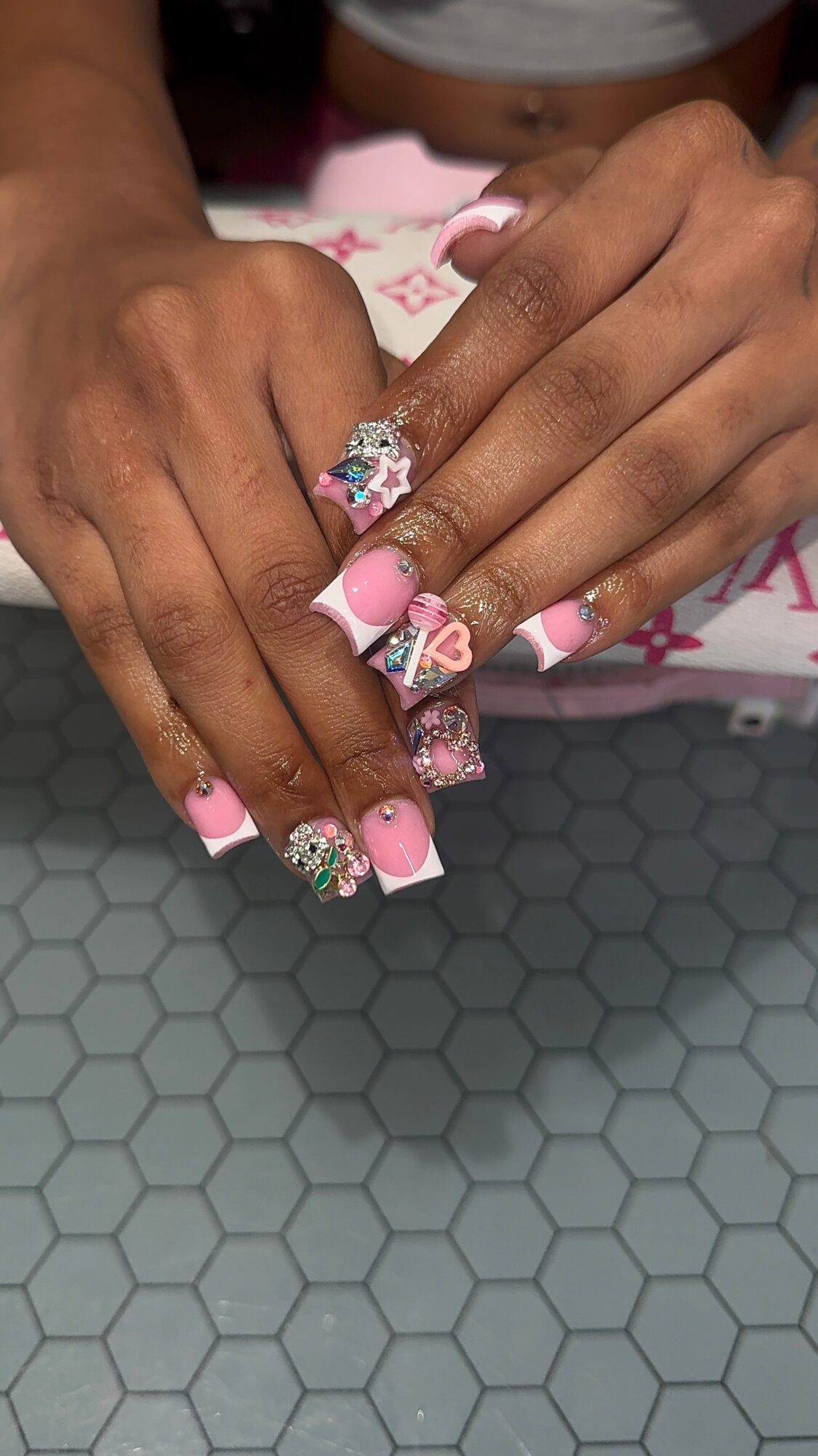 Two hands with decorated nails and a large ring, resting on a hexagonal-pattern surface.
