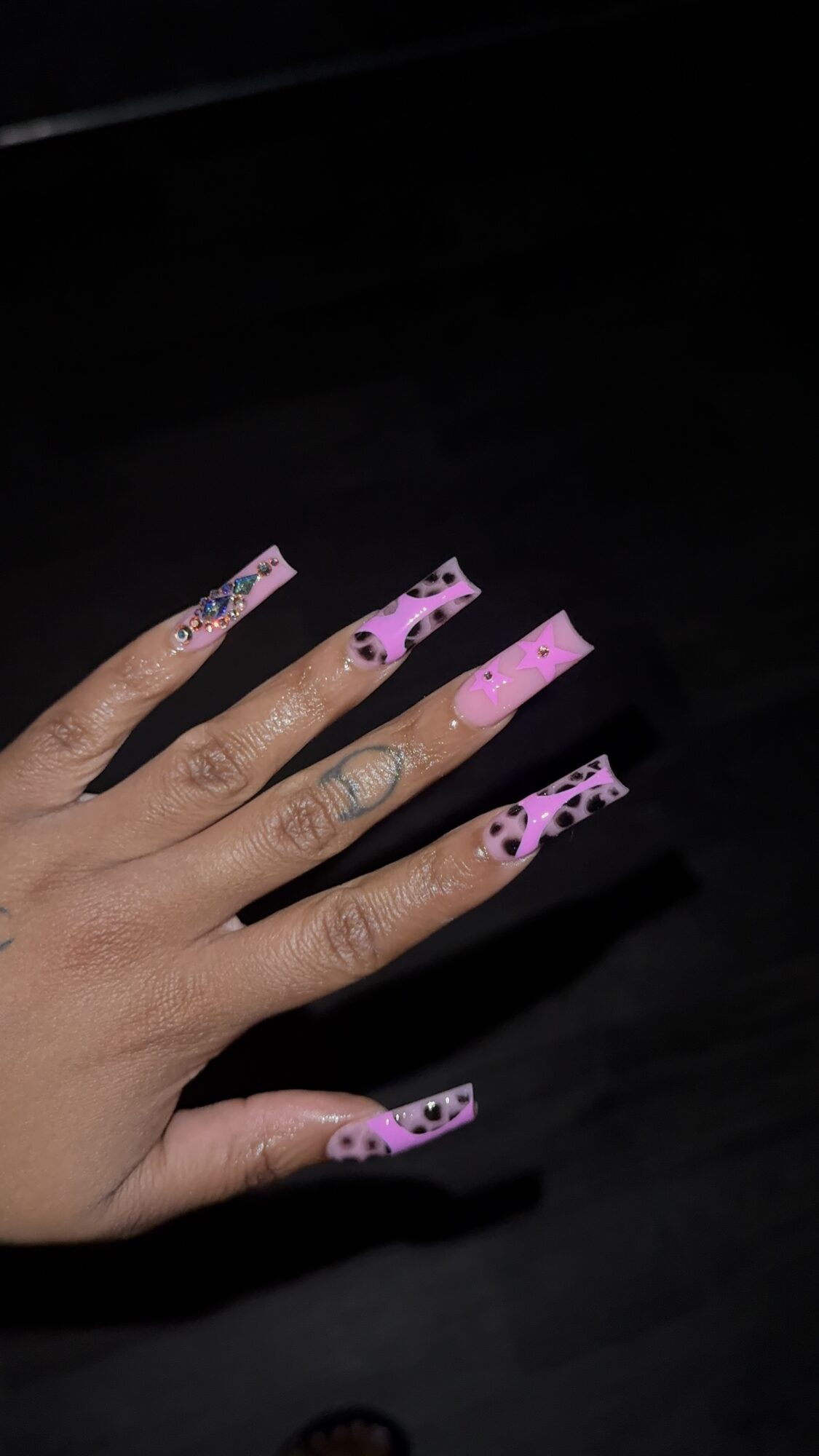 Hand with long, decorated nails resting on a dark surface.