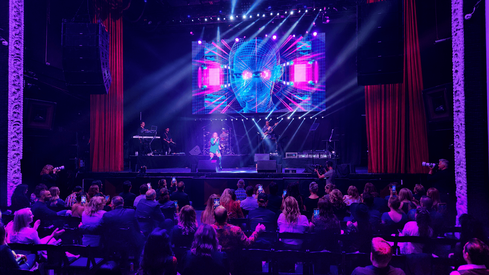 Stage with performers, colorful lights, and audience in a theater setting.
