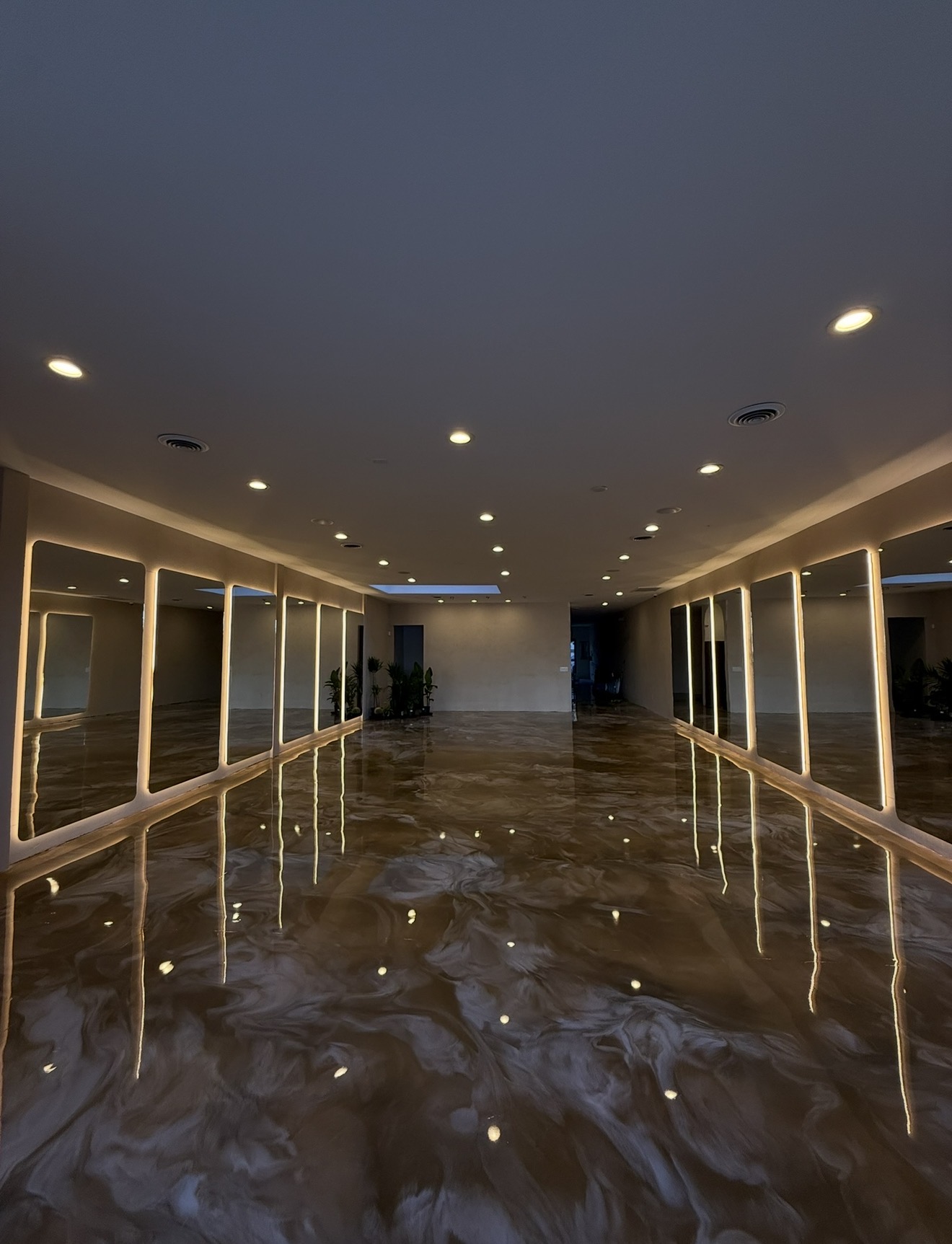 Indoor pool with water reflecting ceiling lights and large windows on both sides, leading to a distant wall.
