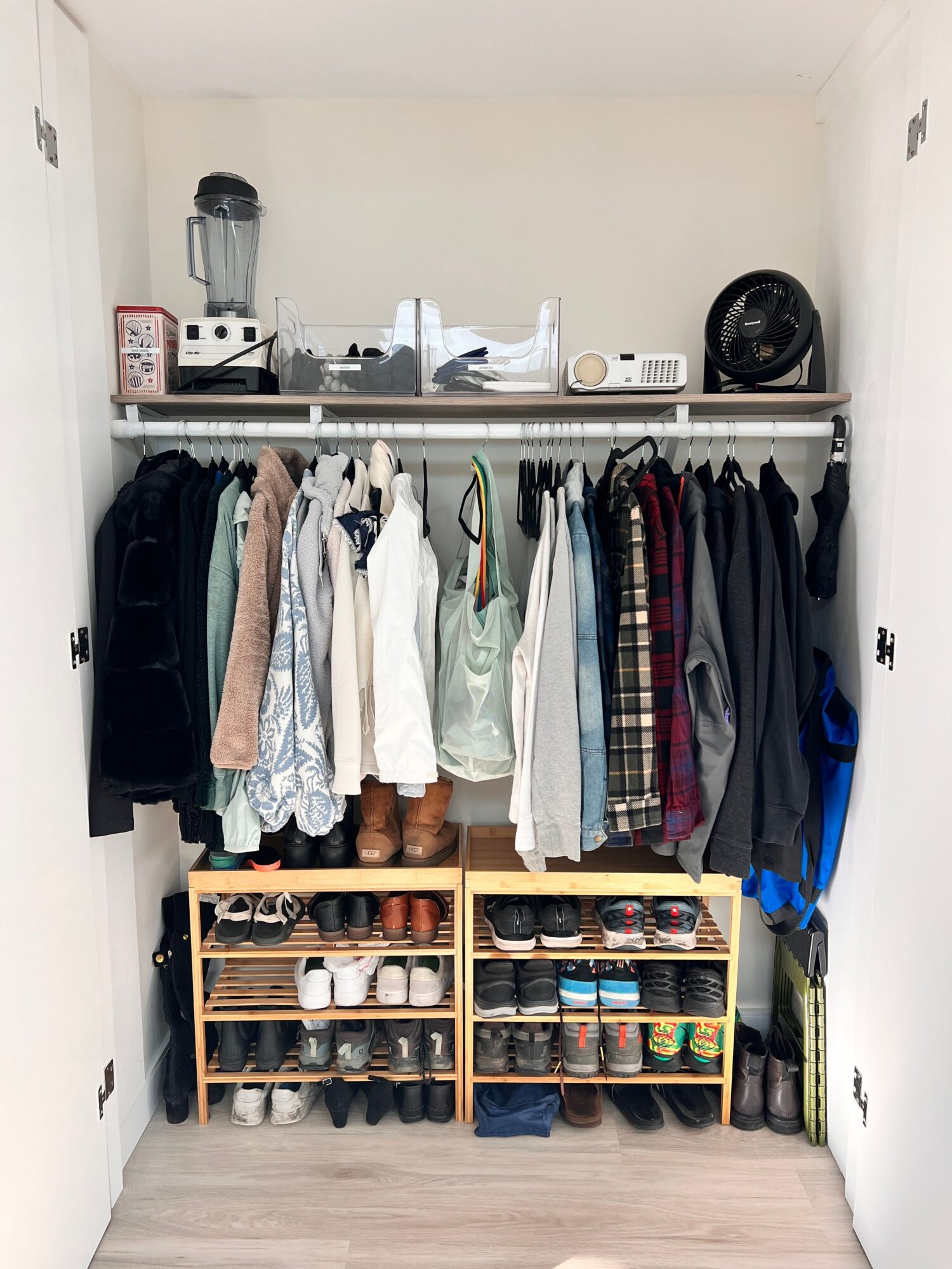 Closet with hanging clothes, shelves with shoes, and a small shelf with bottles, viewed from the side.