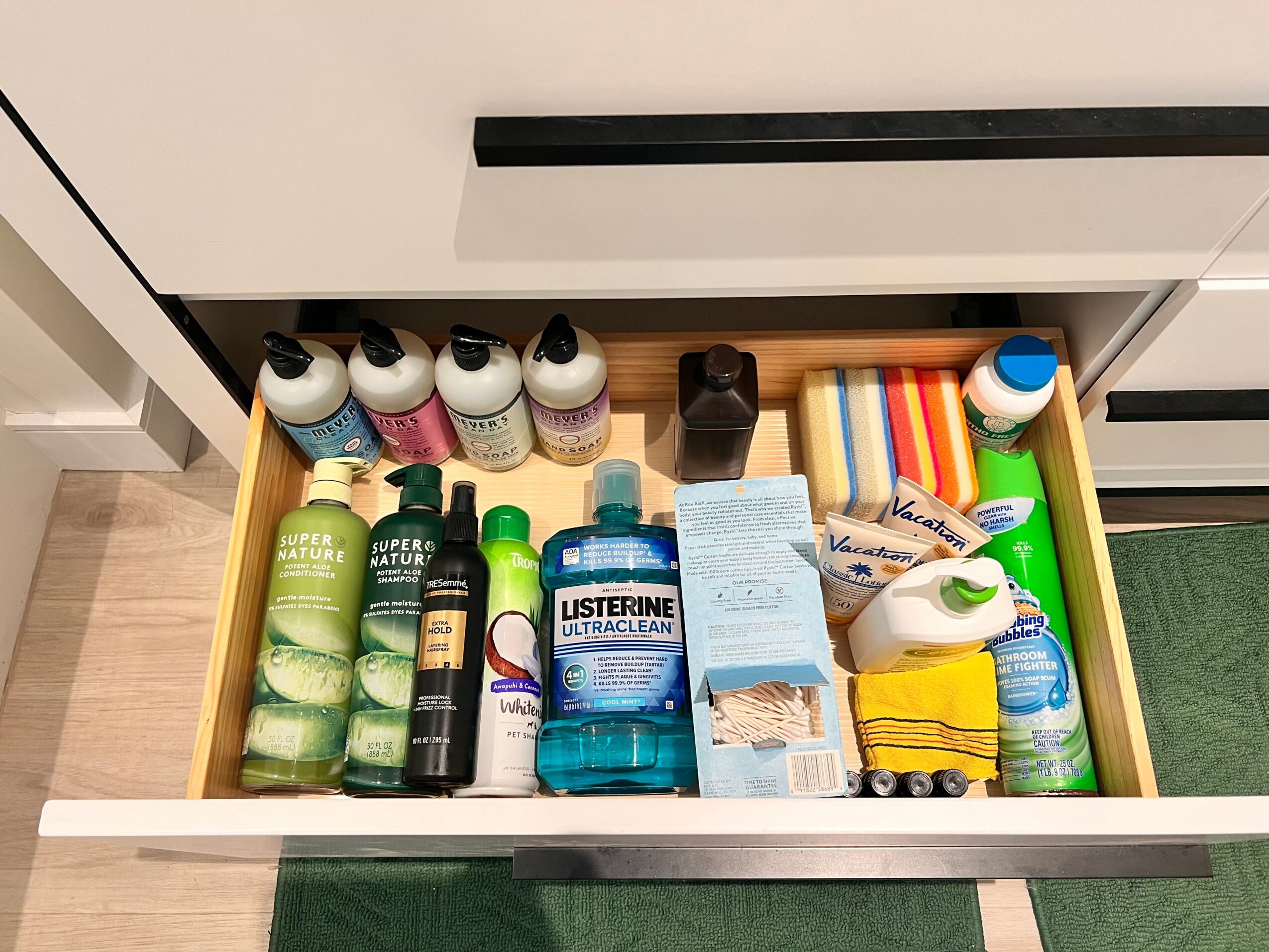 Open drawer with toiletries including bottles, soap, and cleaning supplies, organized neatly.