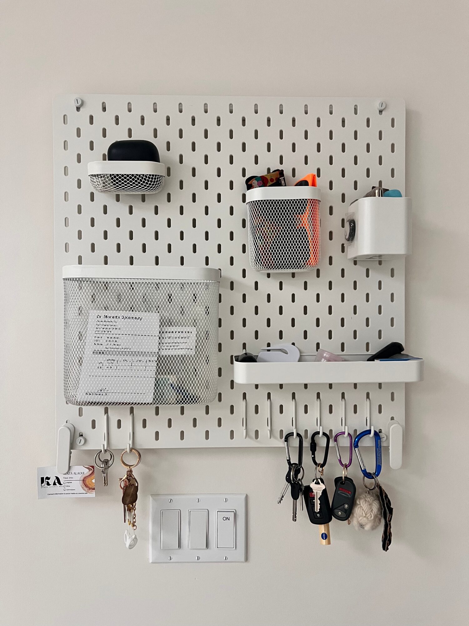 Pegboard with storage containers, hooks, and small items on a white wall.