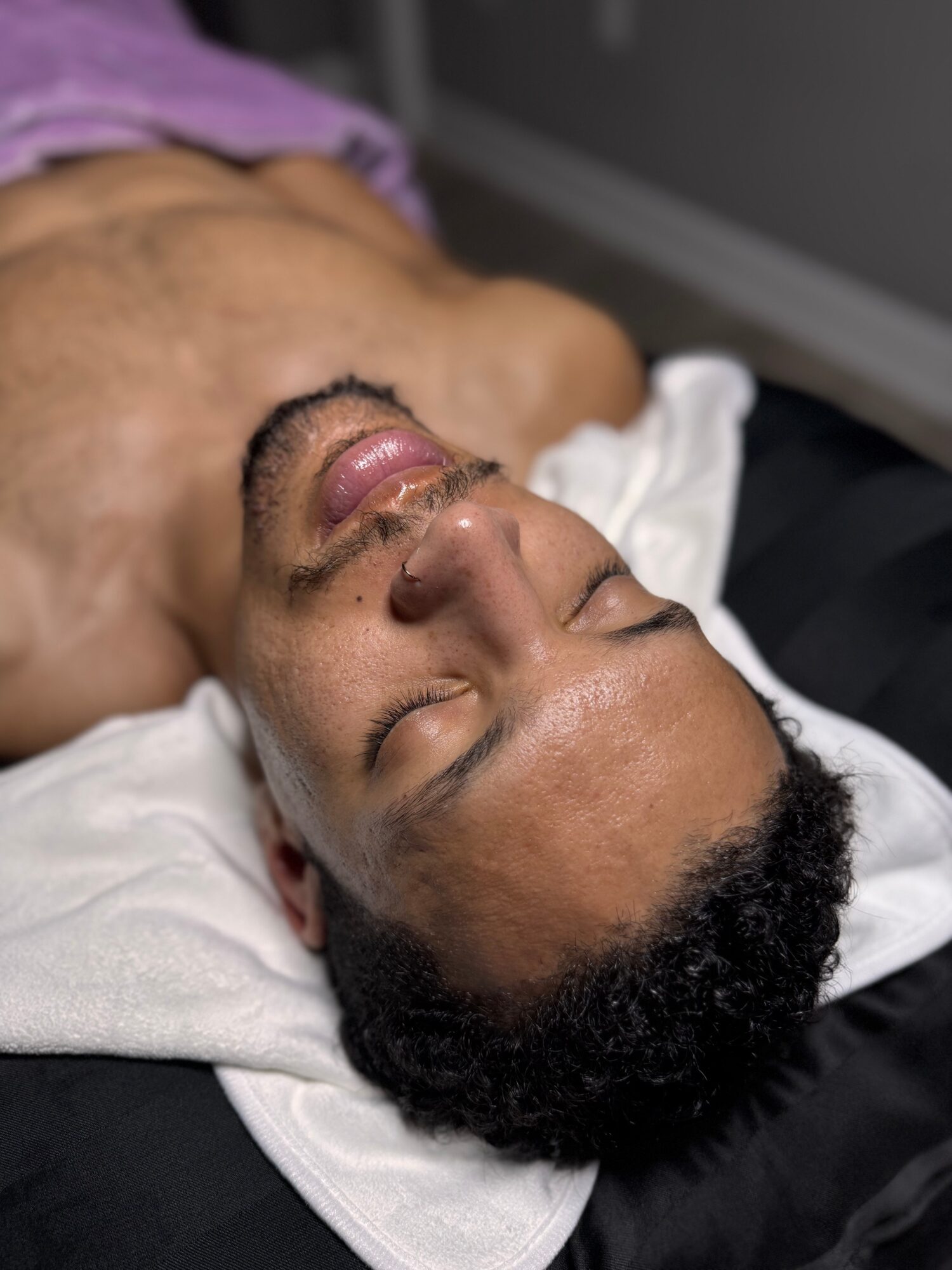 Person lying down with eyes closed, face visible, on a white pillow, with a dark background.