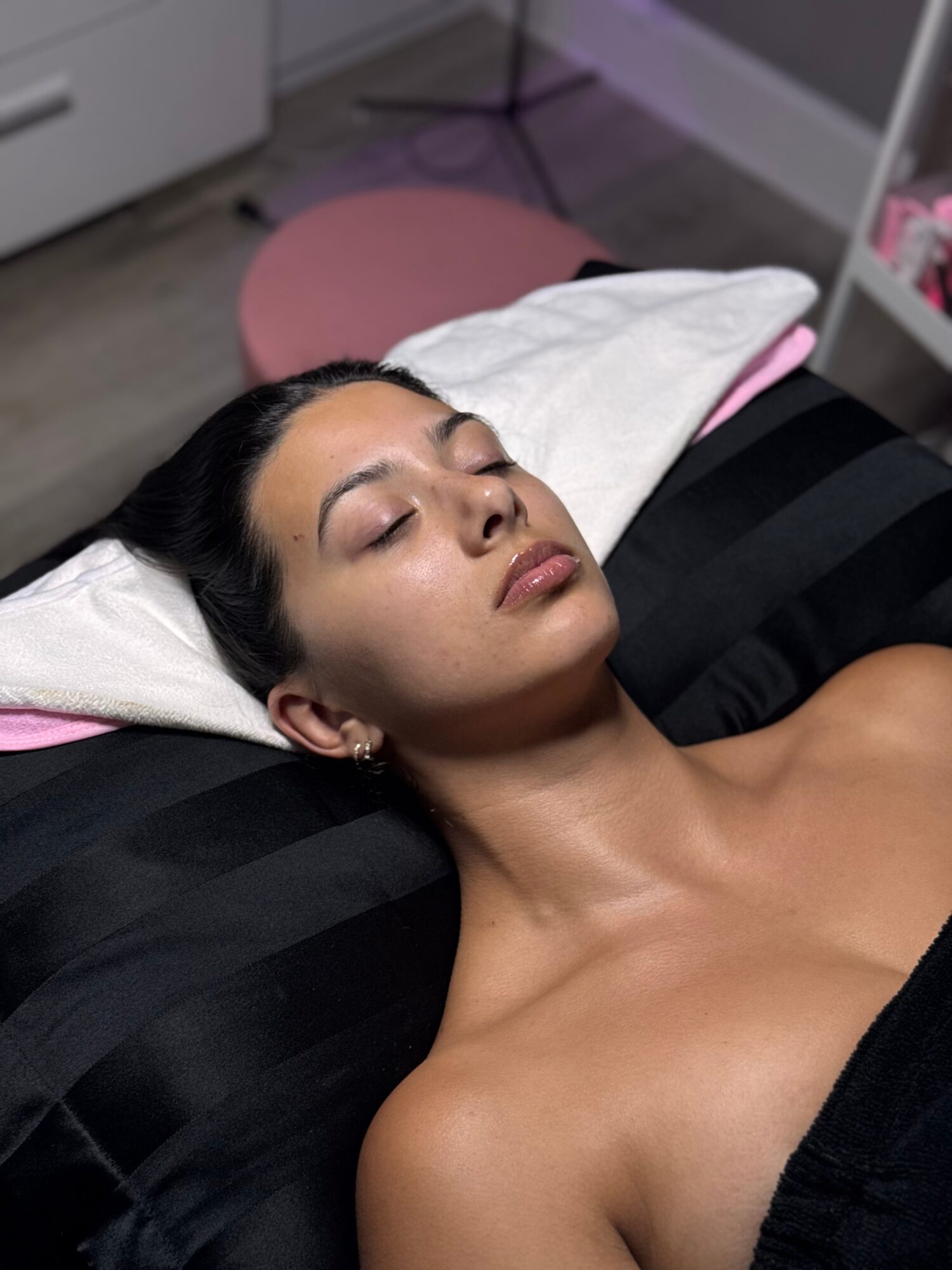 Woman with closed eyes lying on a pillow, relaxed, in a room with a pink mat and white furniture.