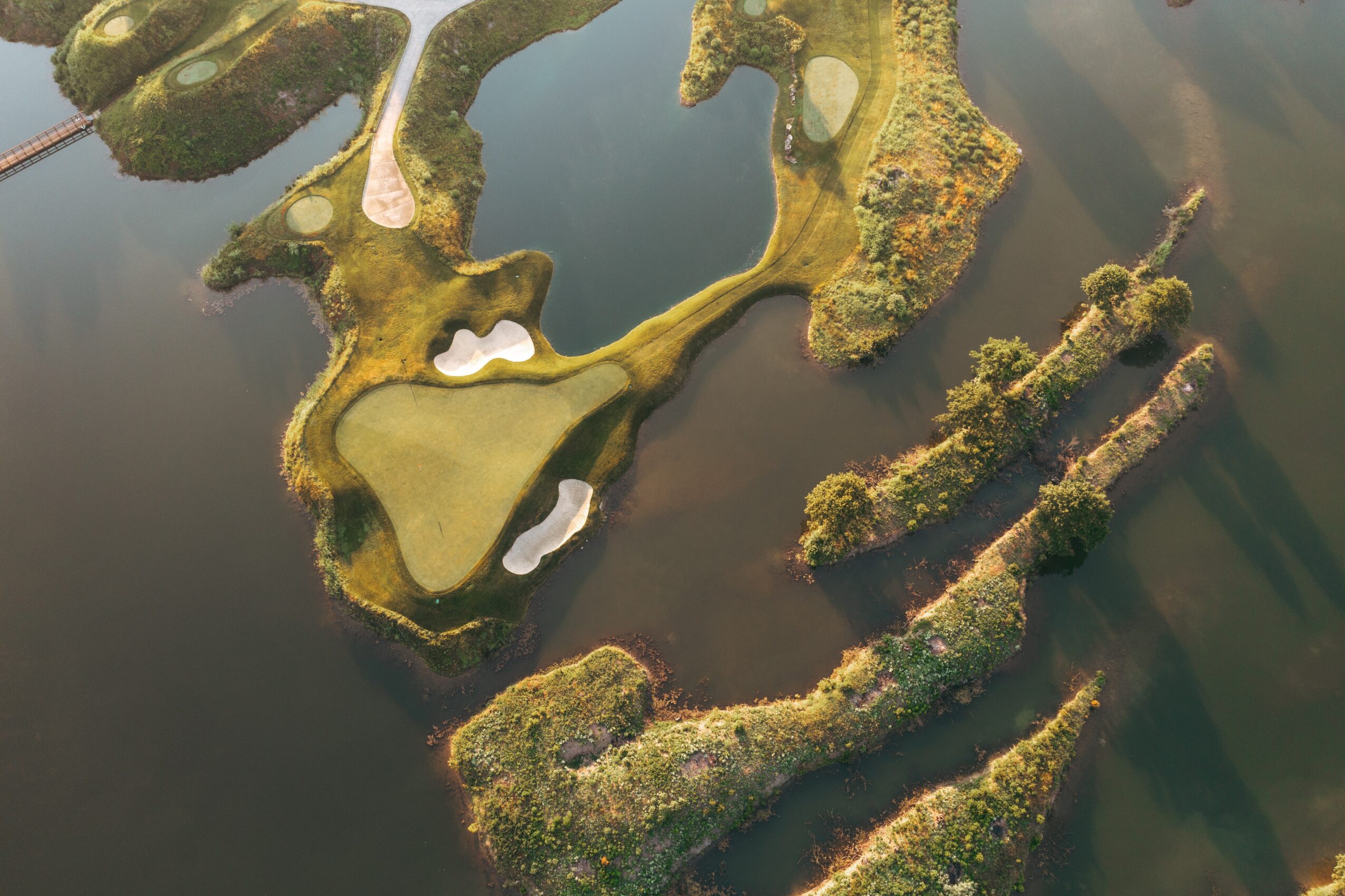 Aerial view of a golf course with water hazards and green fairways, surrounded by trees and natural landscape.