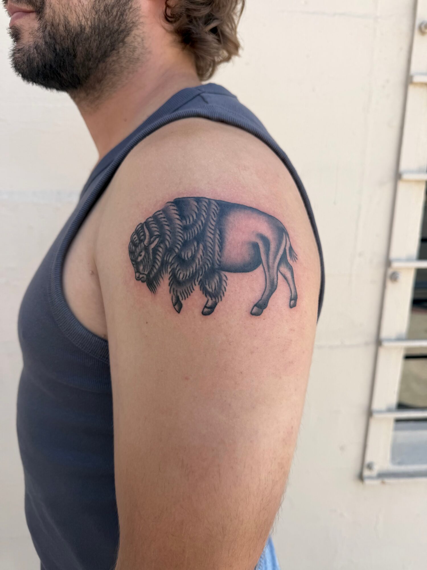 Tattoo of a lion with a detailed mane on person's upper arm, facing left, with a neutral background.