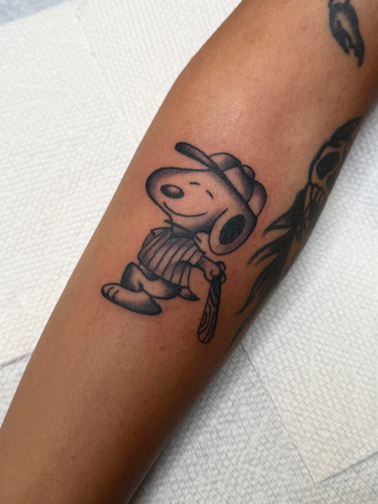 Tattoo of Snoopy wearing headphones and a striped shirt, holding a leash, on a person's arm.