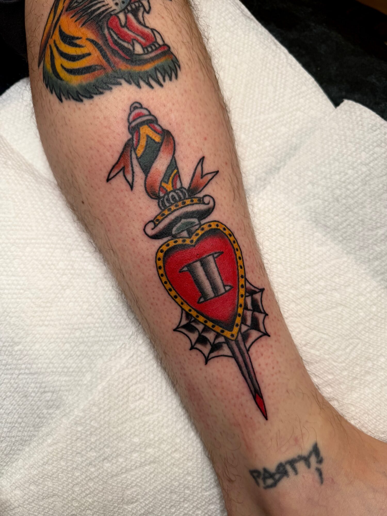 Tattoo of a sword with a shield, snake, and tiger on a person's arm.