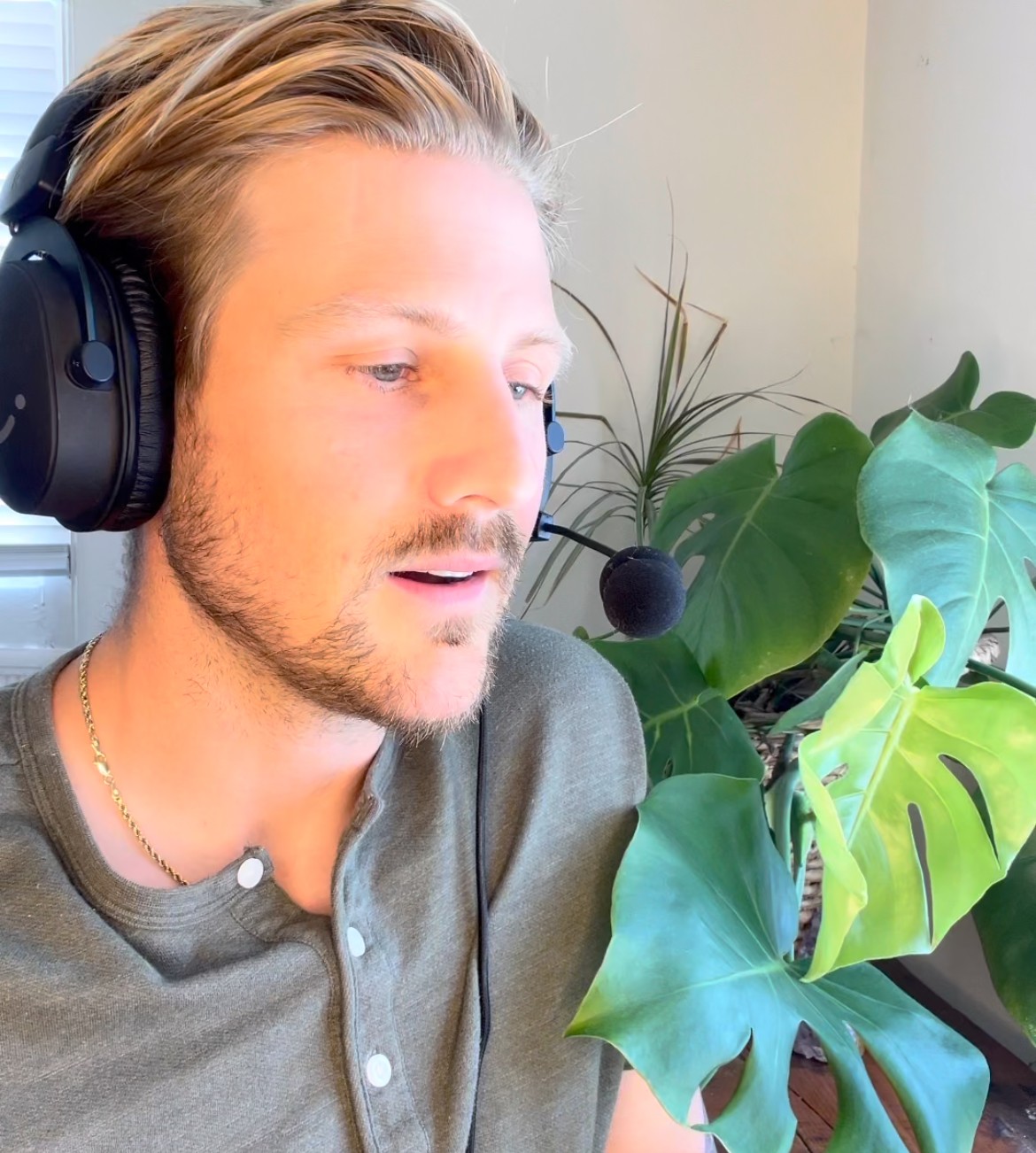 Man with headphones and microphone, looking at a large green plant, in a well-lit room.
