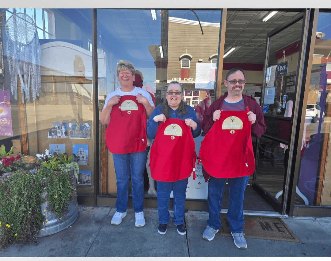 Three people stand outside a store holding red shopping bags, smiling, with glass windows and a door behind them.
