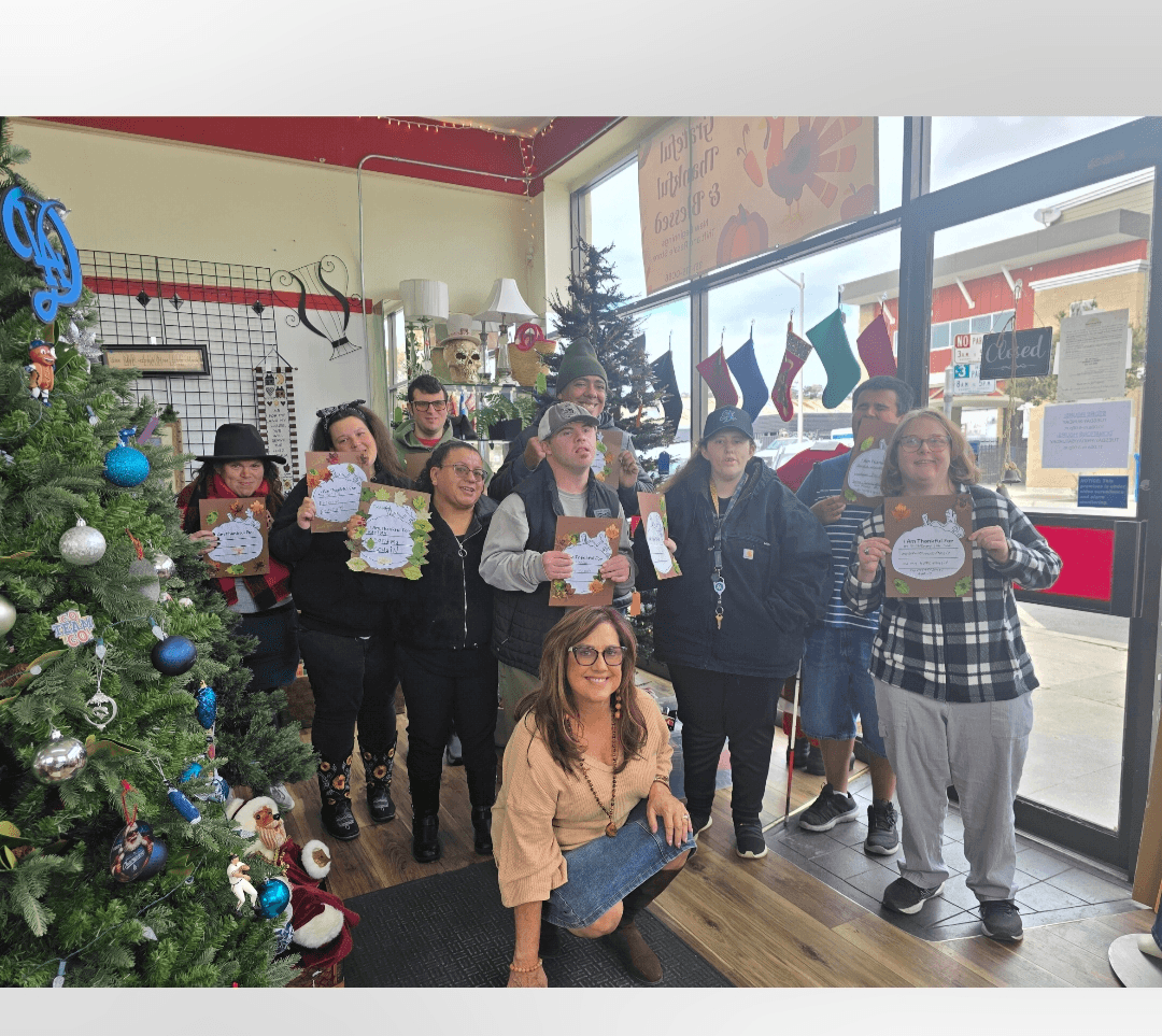 Group of people holding certificates inside a store with Christmas decorations and a large window.