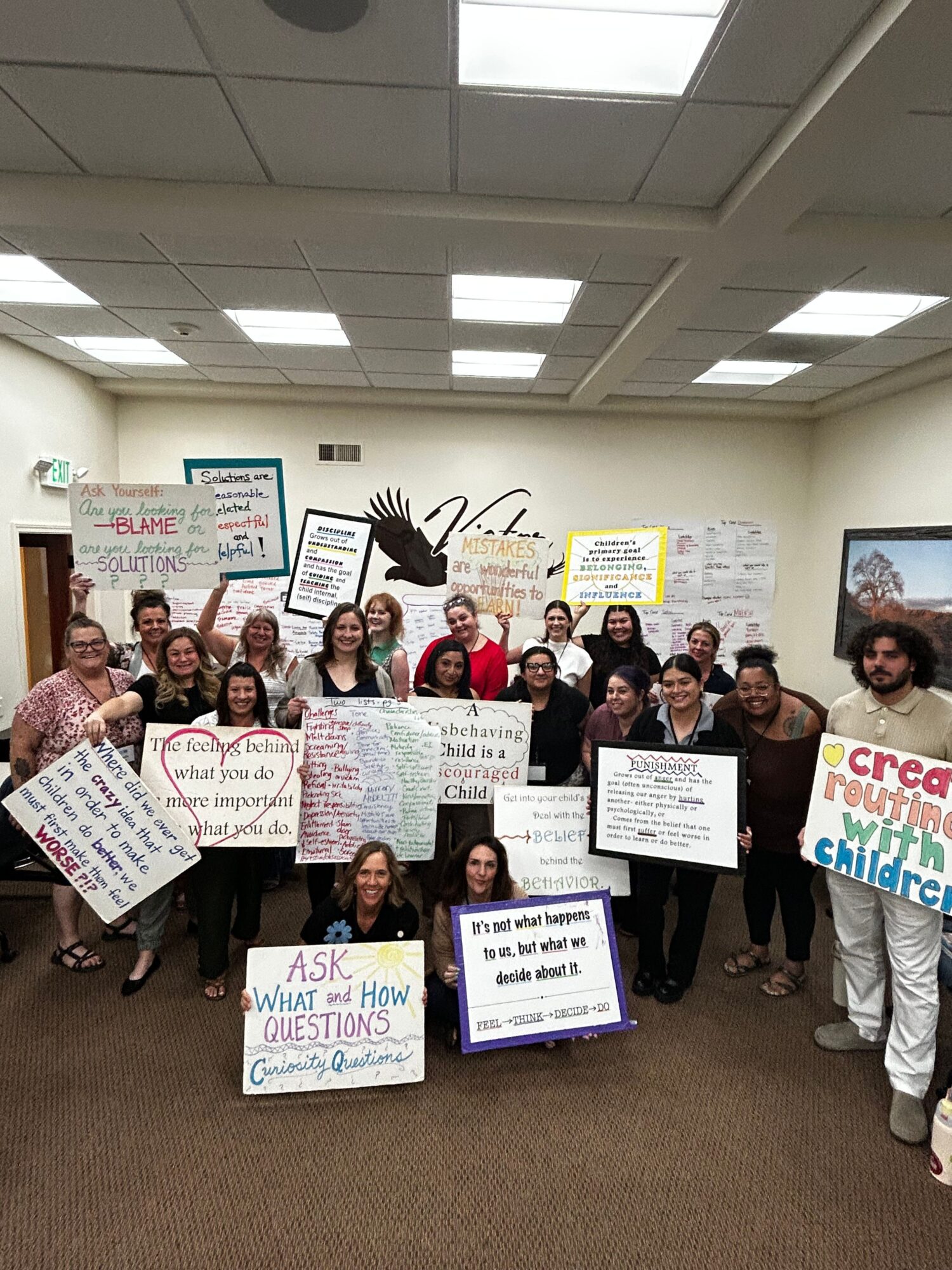 Group of people holding signs in a room with white walls and ceiling lights.