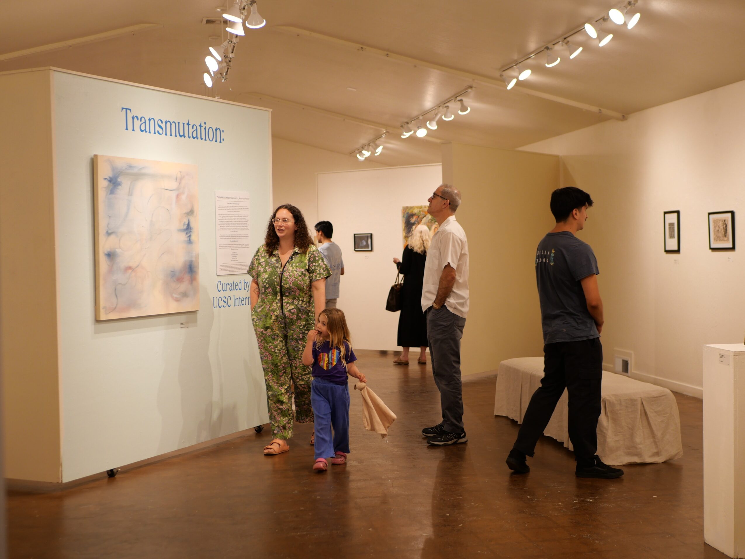 People viewing artwork in an art gallery, including a woman, children, and men, with framed pieces on the walls.