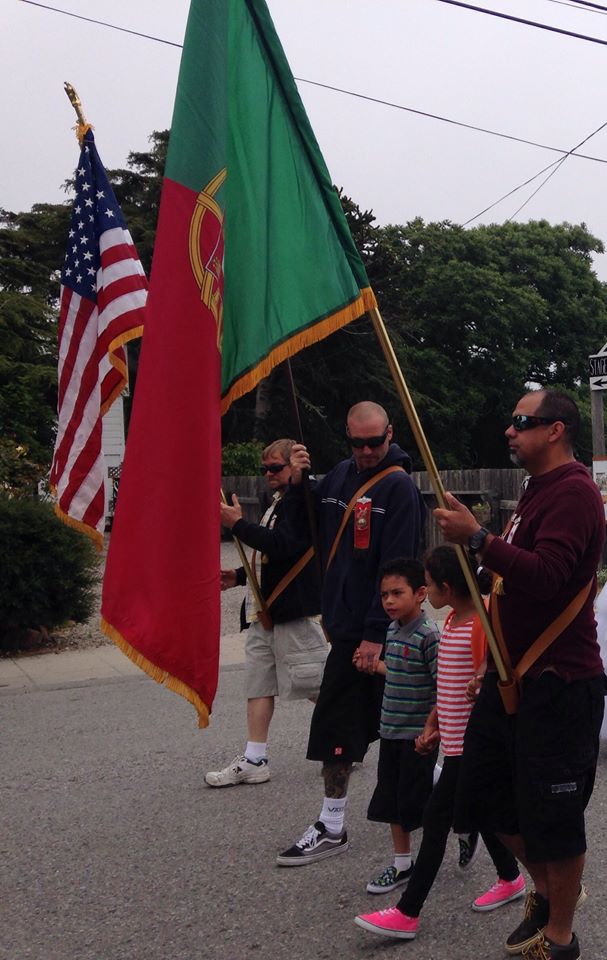 Group of people holding American and military flags during a parade or event, with trees and power lines in background.