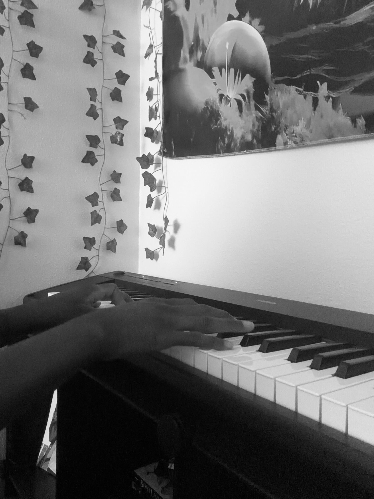 Person's hand playing piano keys, wall with ivy and a space-themed poster in the background.