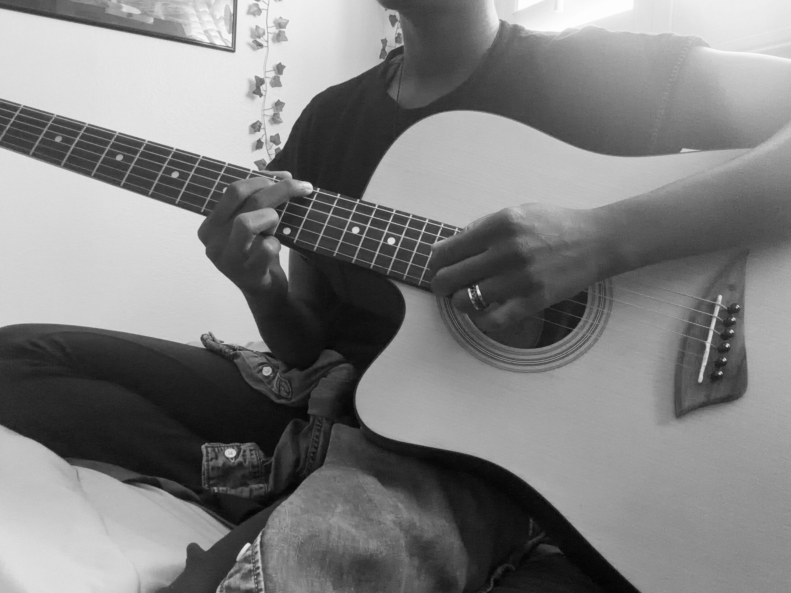 Person playing an acoustic guitar, focusing on hands and guitar body, in a room with wall decorations.