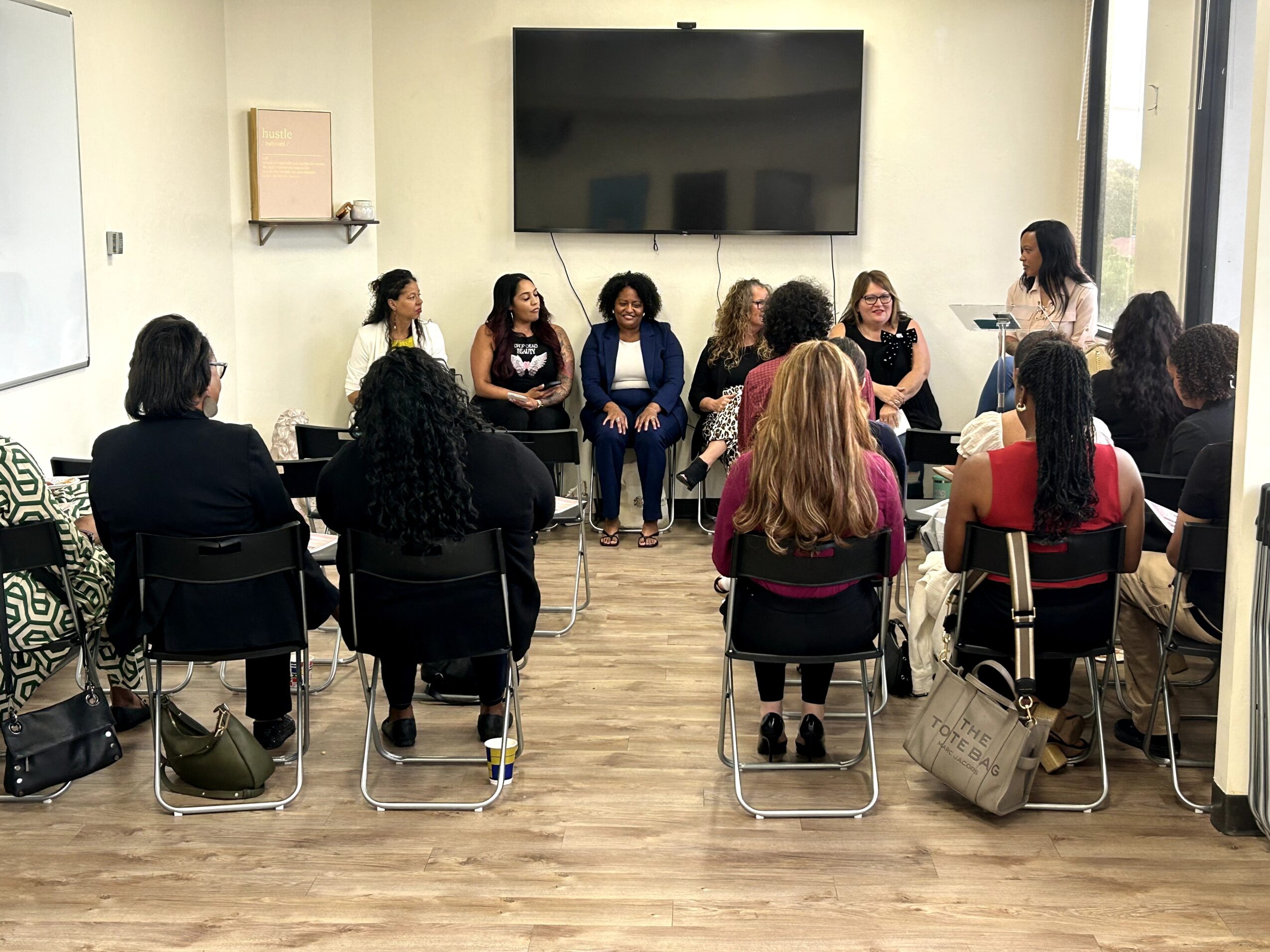 Group of women sitting in a circle during a discussion in a room with a large screen on the wall.