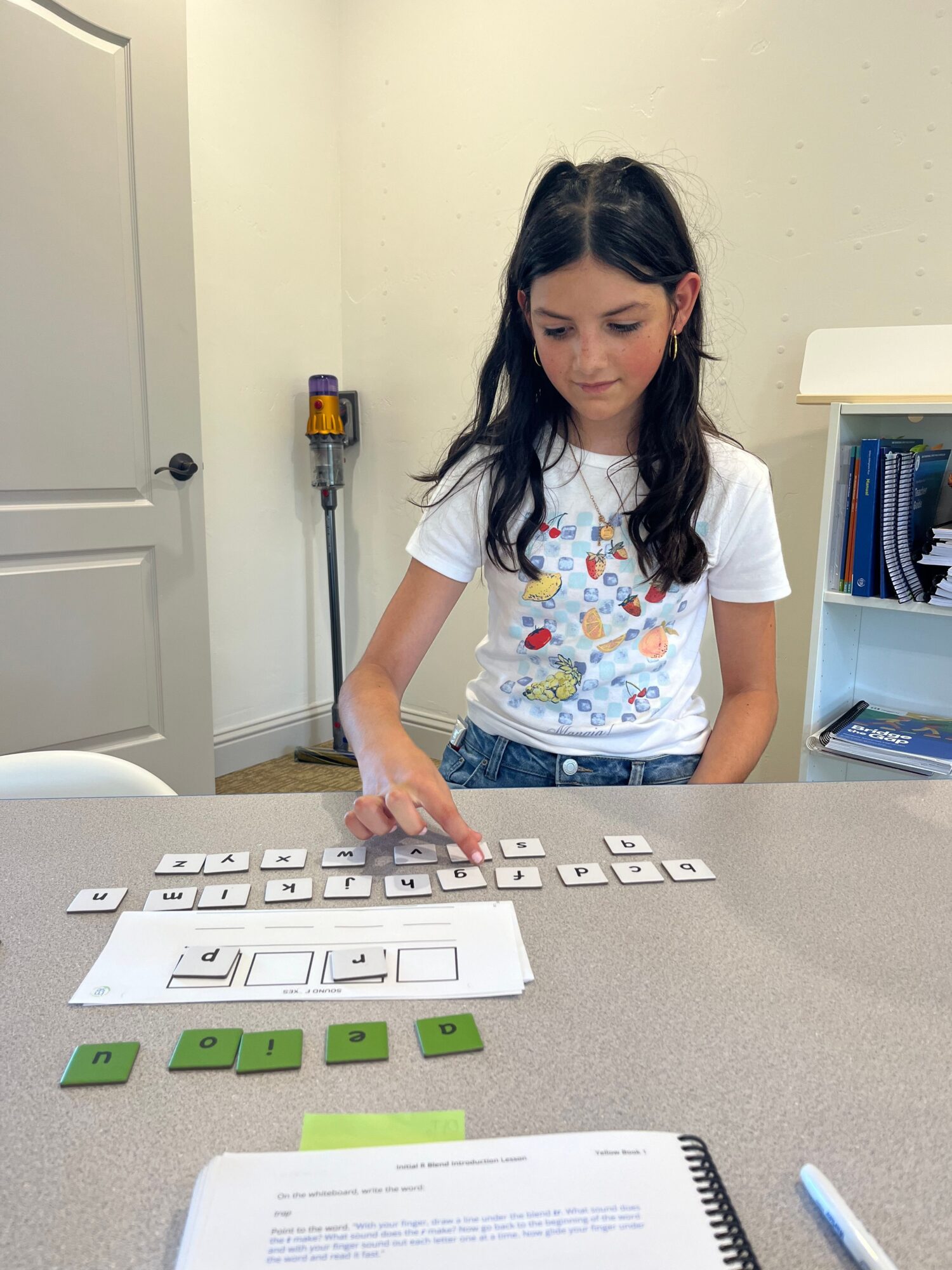 Girl with long dark hair wearing a white shirt and colorful apron, reaching for keyboard keys on table.