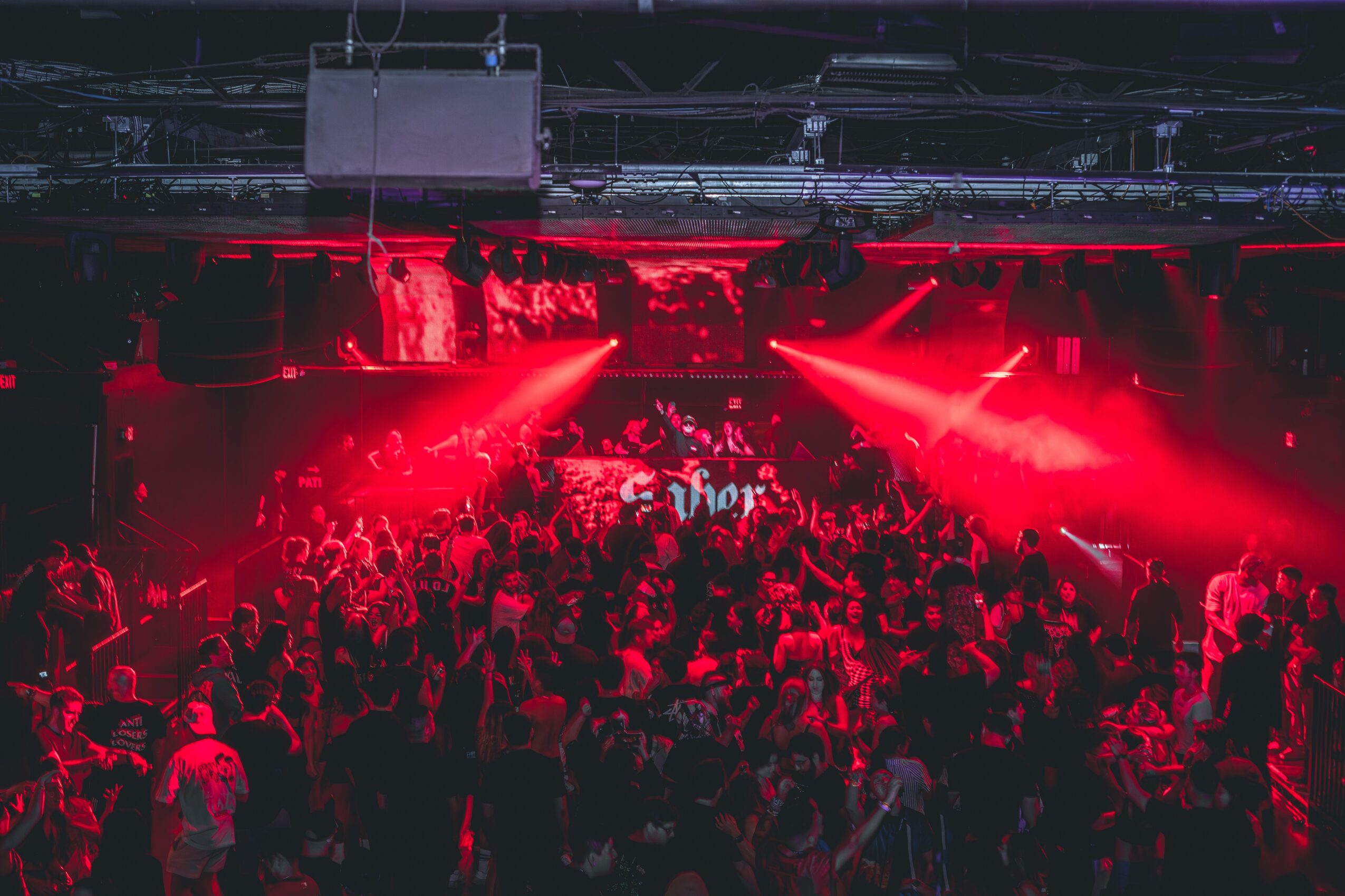 Crowd of people at a concert with red stage lighting and a dark background.
