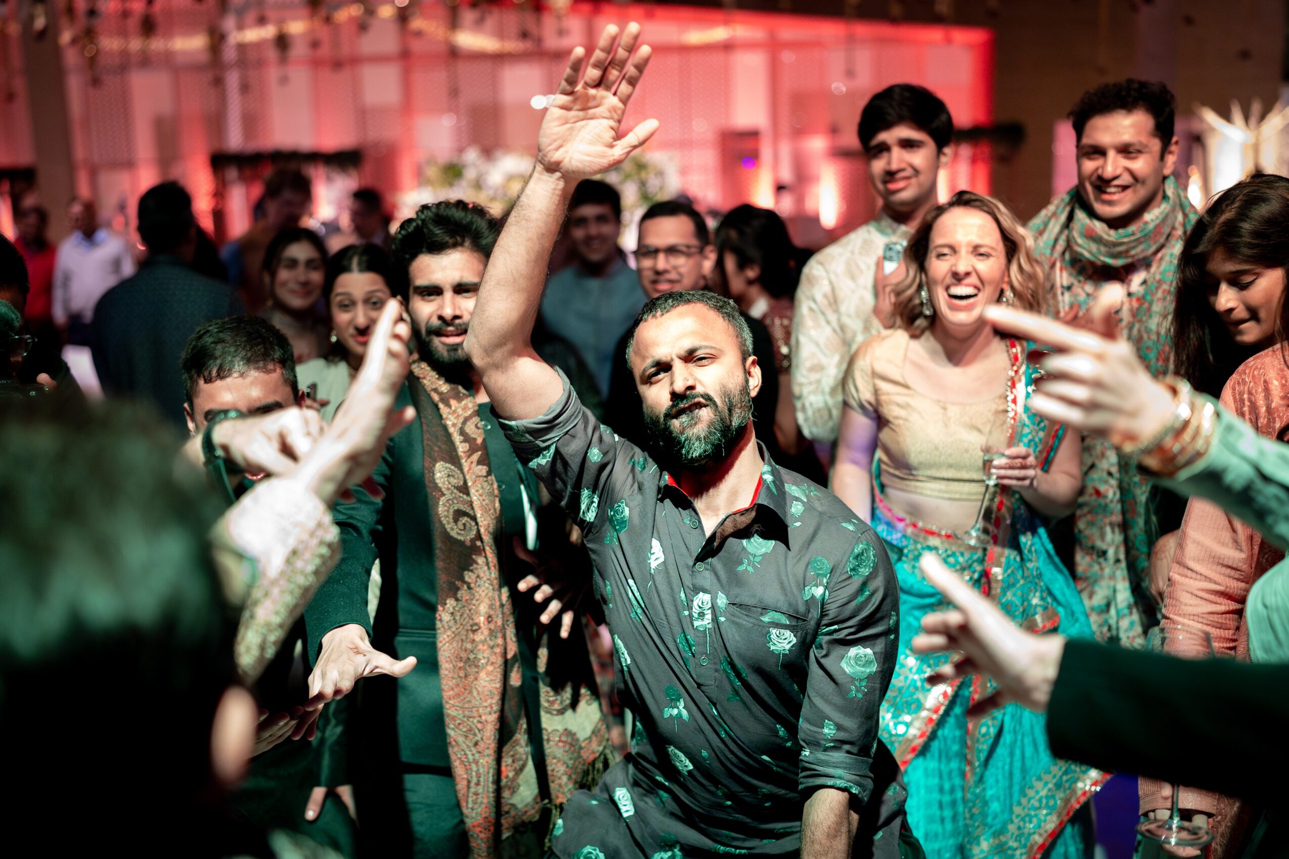 Group of people celebrating and smiling at a party with colorful lighting, some raising hands and others clapping.