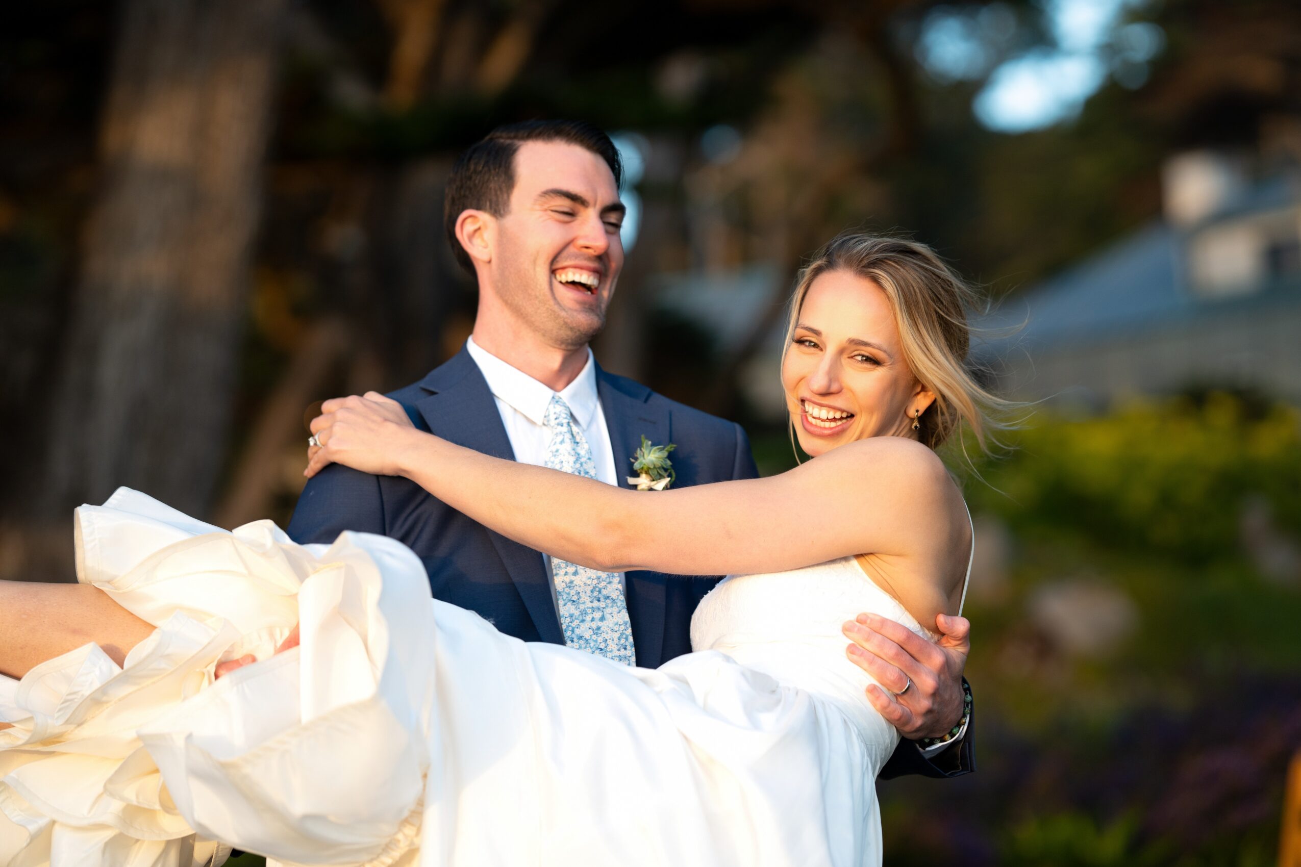 A happy couple, the man in a suit and the woman in a wedding dress, smiling and embracing outdoors.