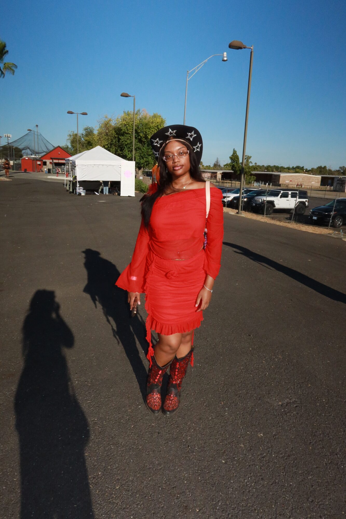 Woman in red dress and black hat standing on asphalt road with parking lot and blue sky background