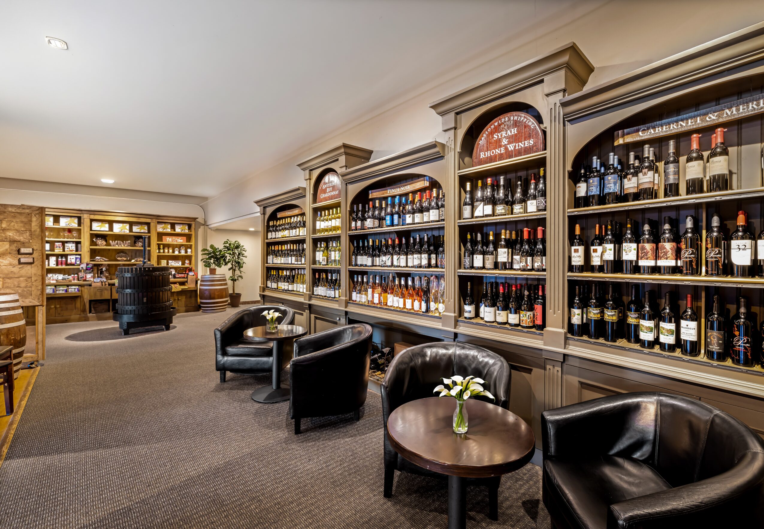 Elegant room with bookshelves filled with bottles, black chairs, small tables, and a bookshelf in the background.