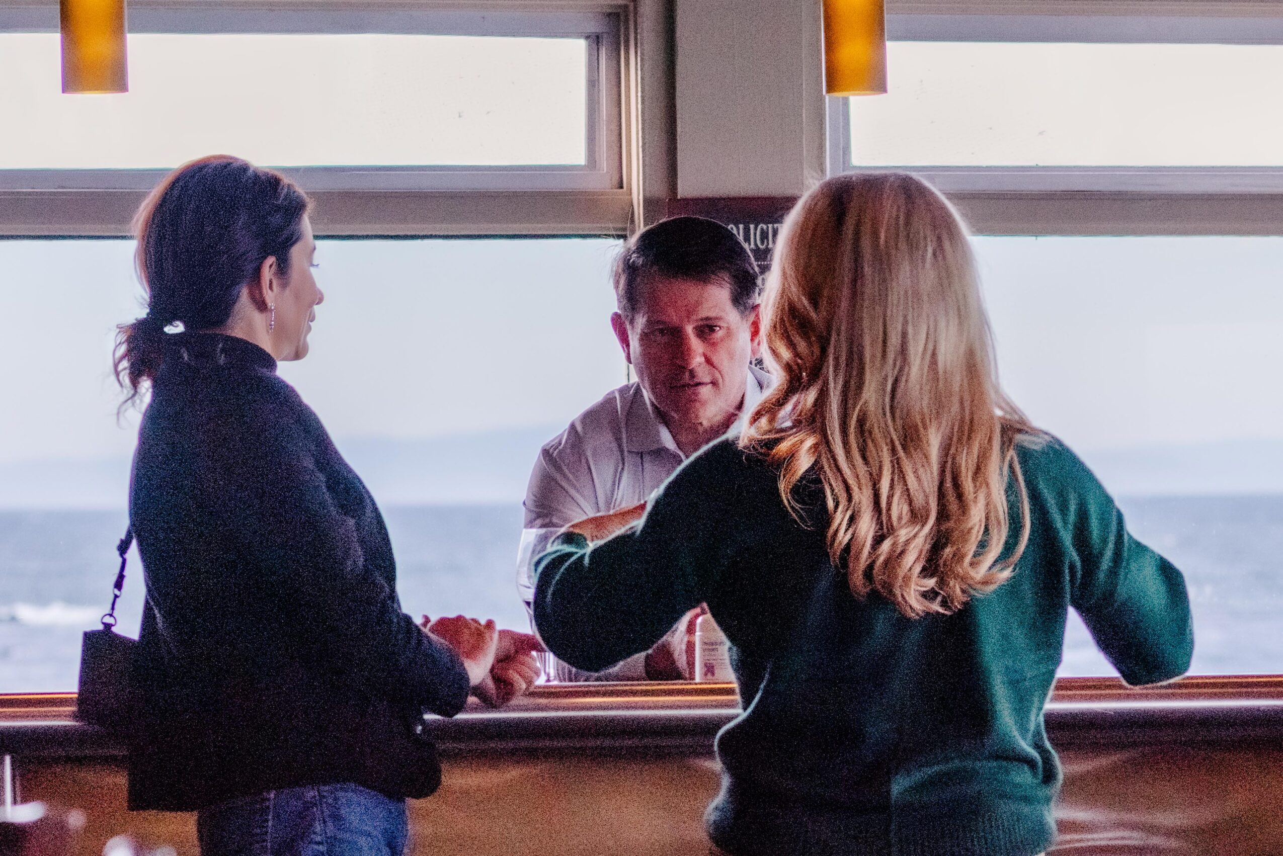 Three people standing near a window, engaging in conversation indoors.