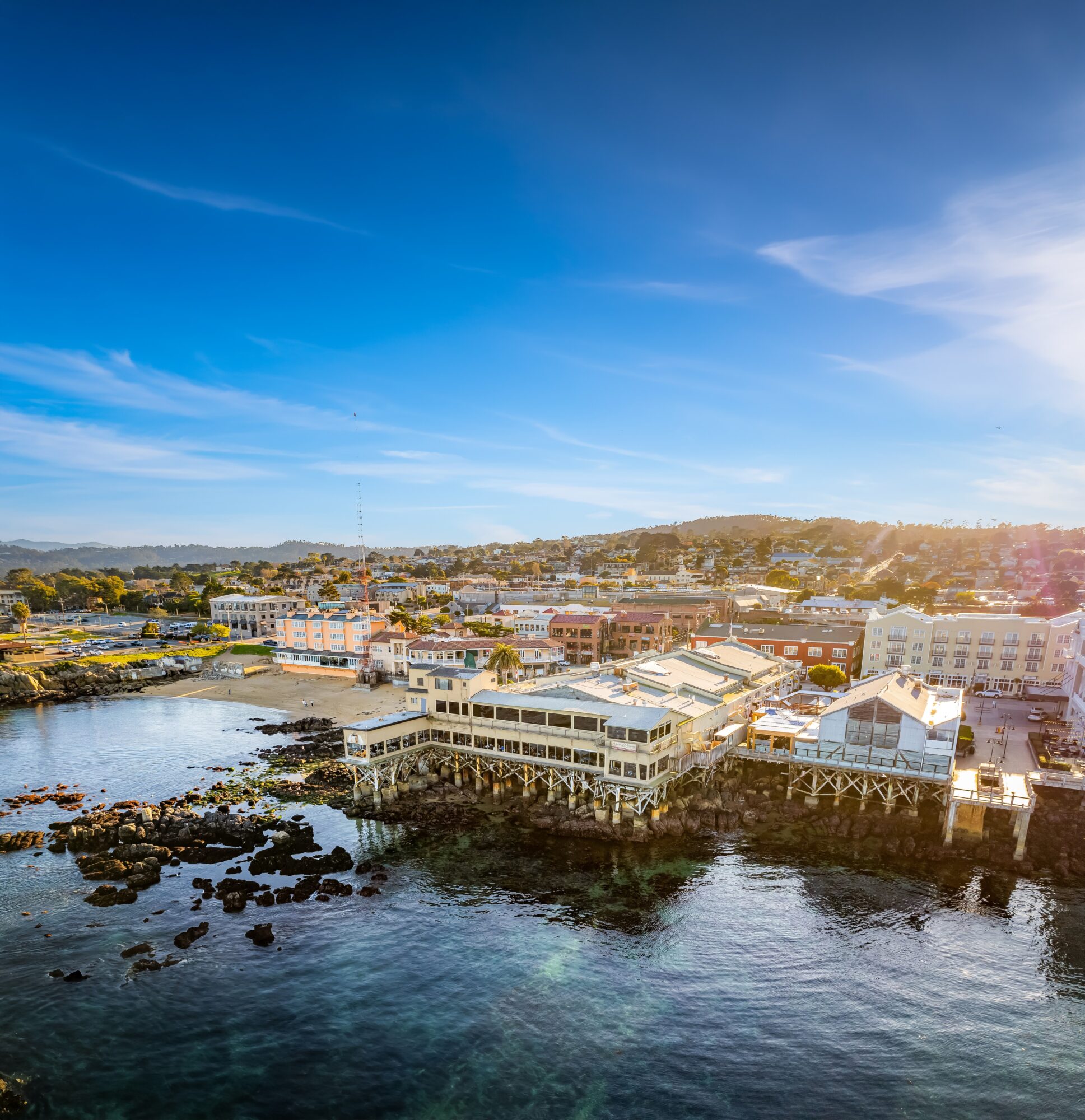 A coastal town with buildings along the water, under a blue sky with some clouds.