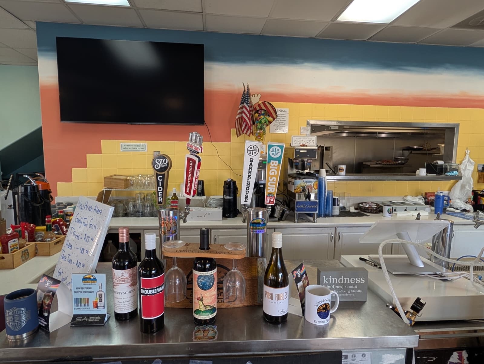 Counter area with drinks, a mug, and a colorful mural in the background, including a TV screen and kitchen opening.