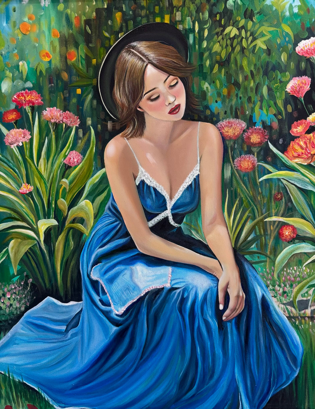 Young woman in a blue dress sitting among colorful flowers and greenery, wearing a black hat, with eyes closed.