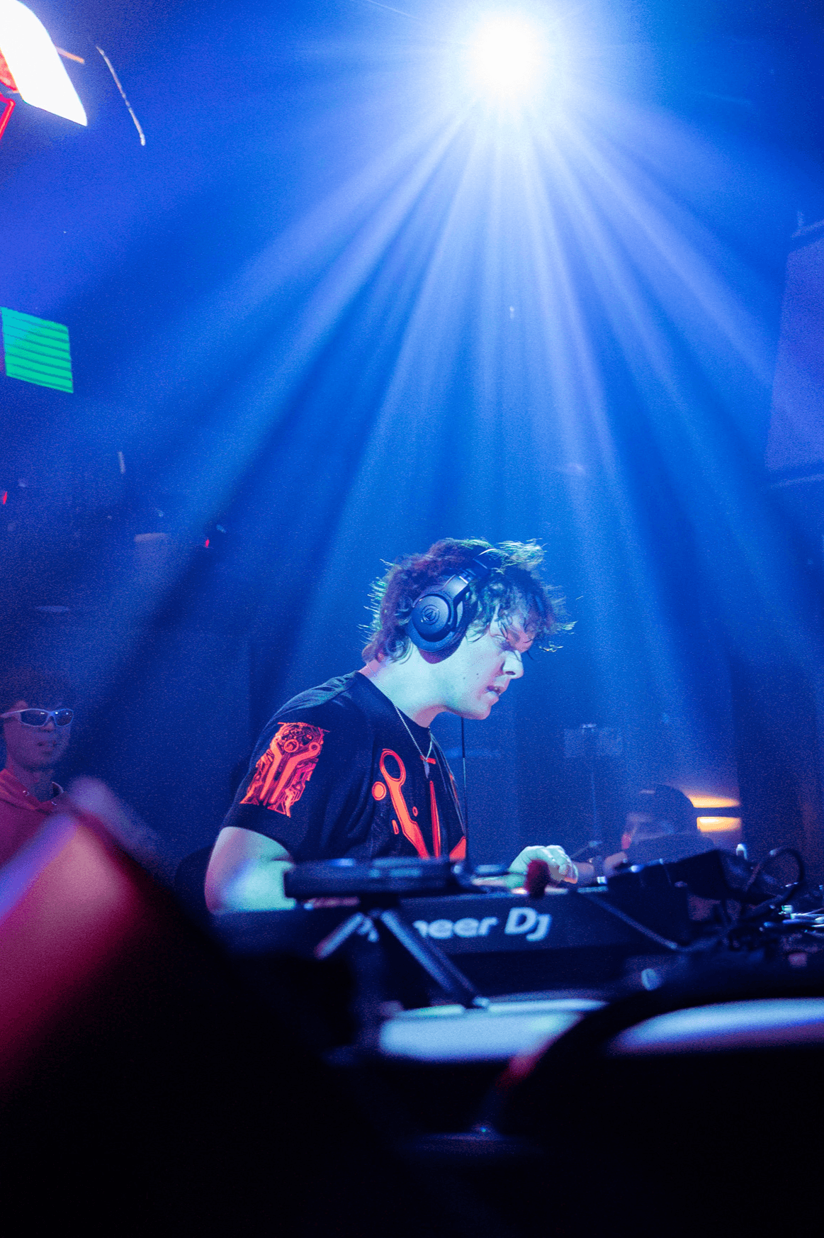 DJ with headphones operating equipment under blue stage lights, focused on mixing, in a nightclub setting.