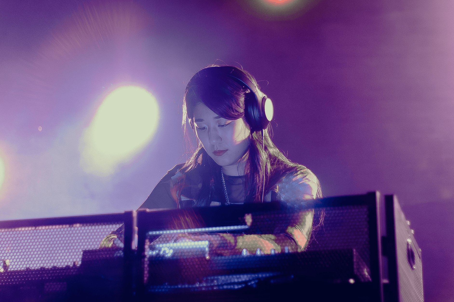 A woman wearing headphones is DJing at a club with colorful lights in the background.