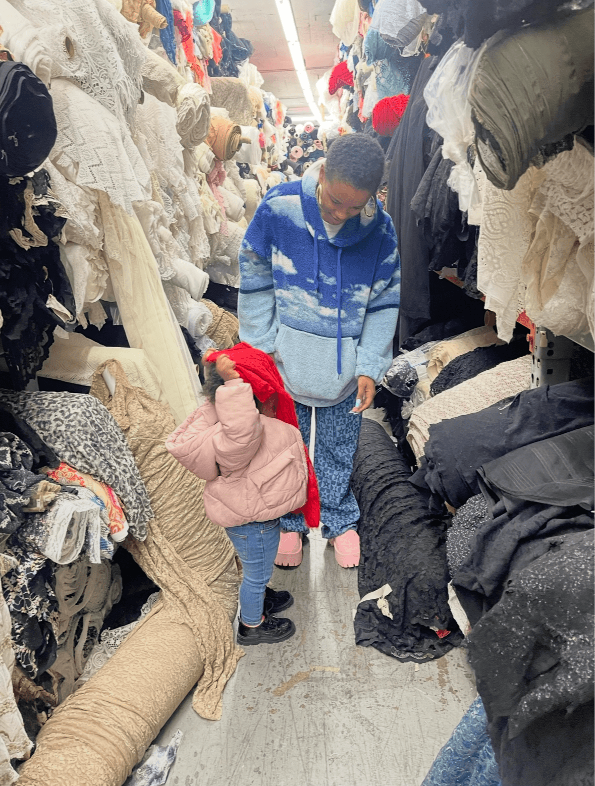 Two children shopping among fabric rolls and textiles in a busy market aisle.